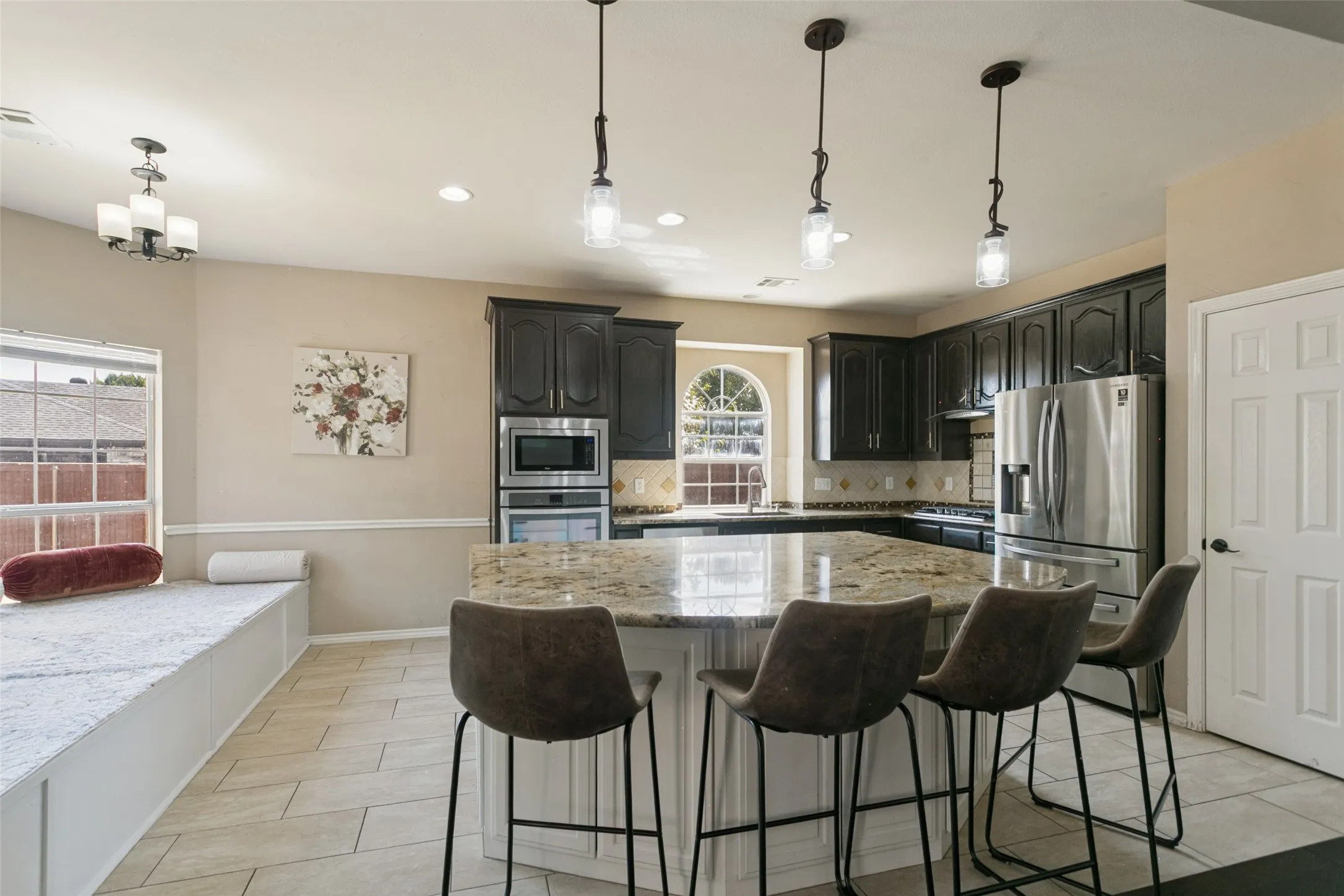 Kitchen featuring a large island with stone countertop, stainless steel appliances, dark wood cabinetry, and a built-in window seat