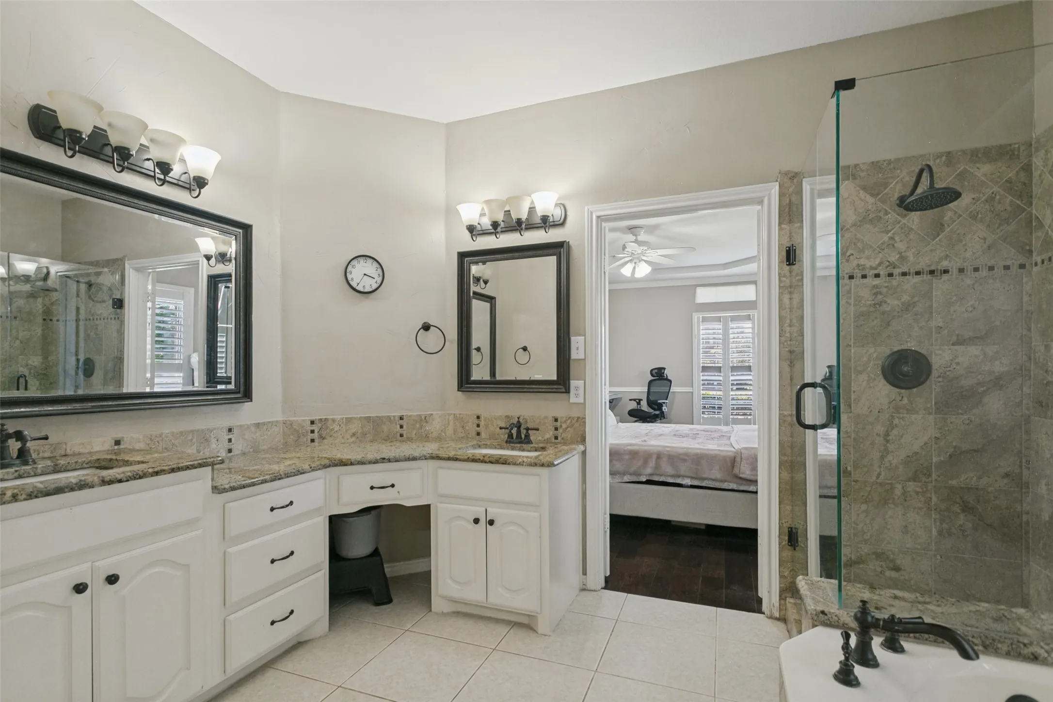 Dual vanity with integrated sinks, ample counter space, custom cabinetry, large walk-in shower with glass enclosure, and tiled flooring
