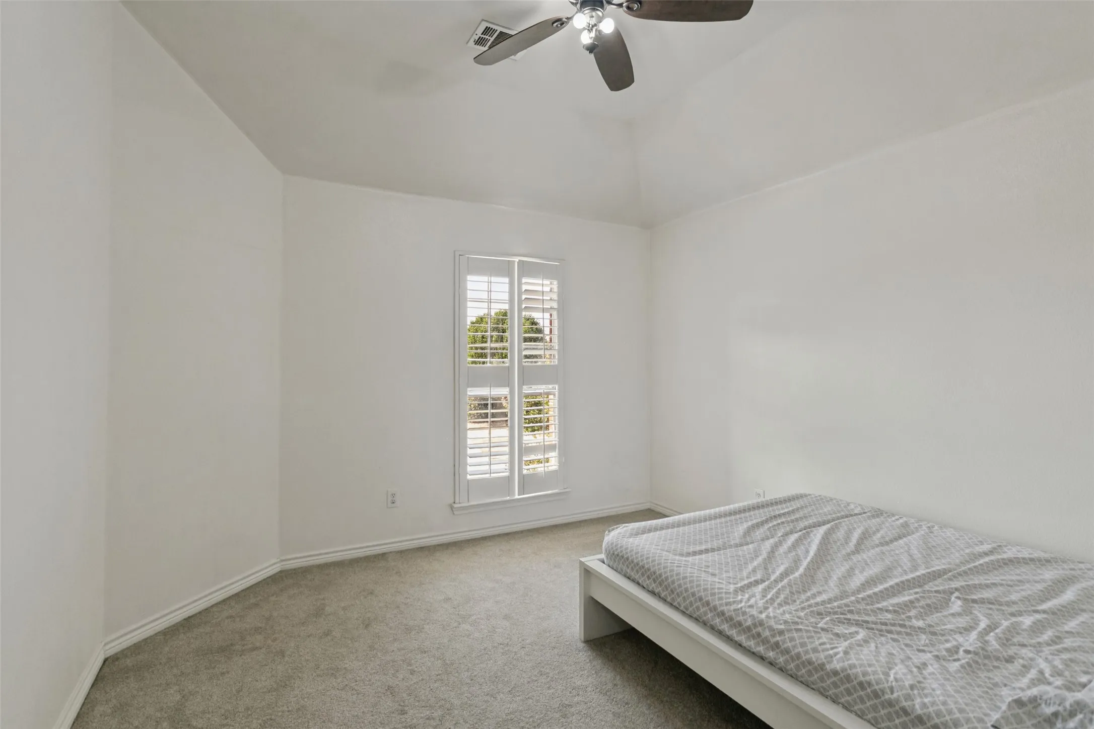 Vaulted ceiling with a ceiling fan, window with plantation shutters, and carpeted flooring