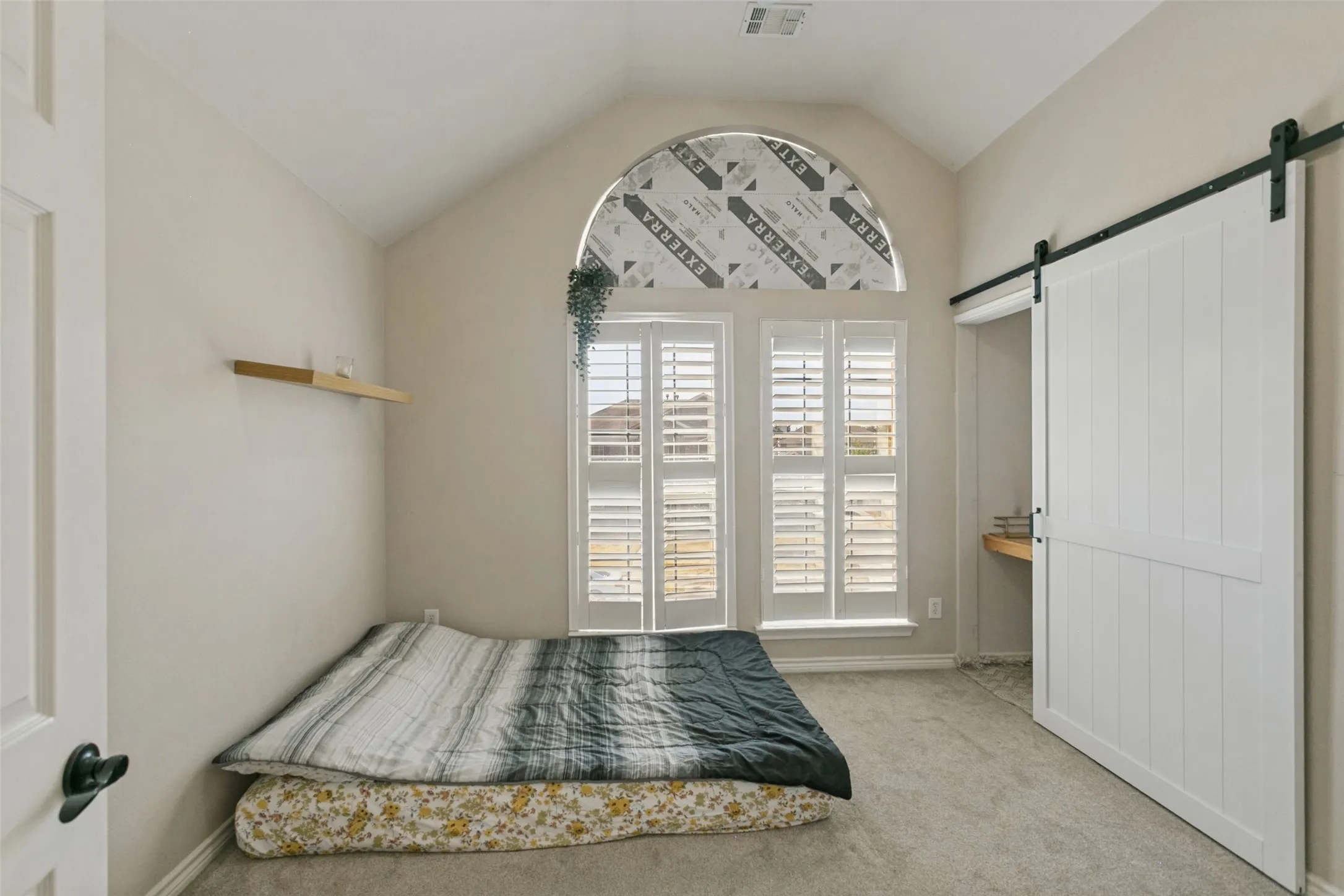 Vaulted ceiling with an arched window, plantation shutters, white paneled barn door, and a floating wood shelf