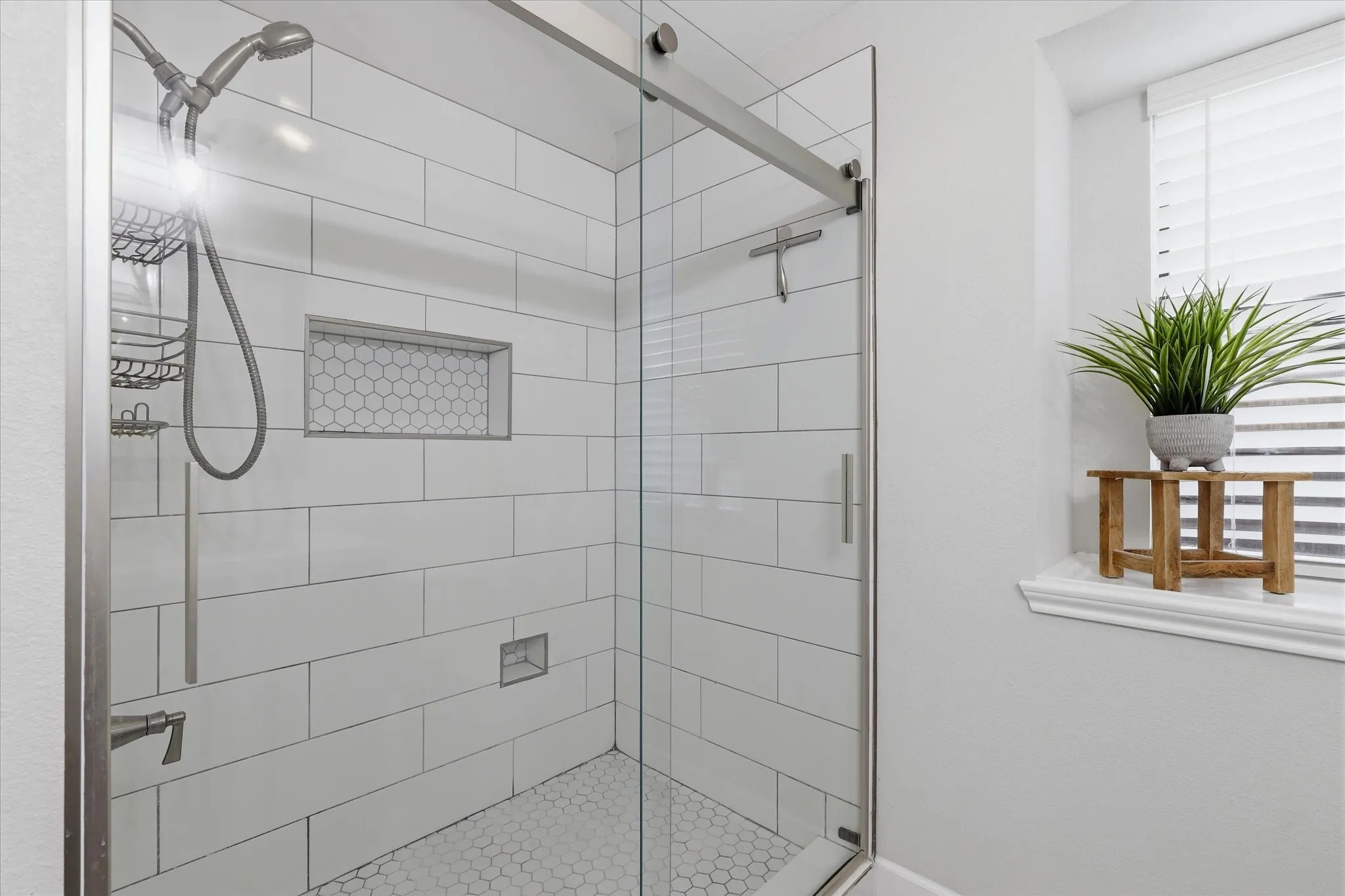 Renovated walk-in shower features frameless glass, oversized tile surround and a decorative tile niche.