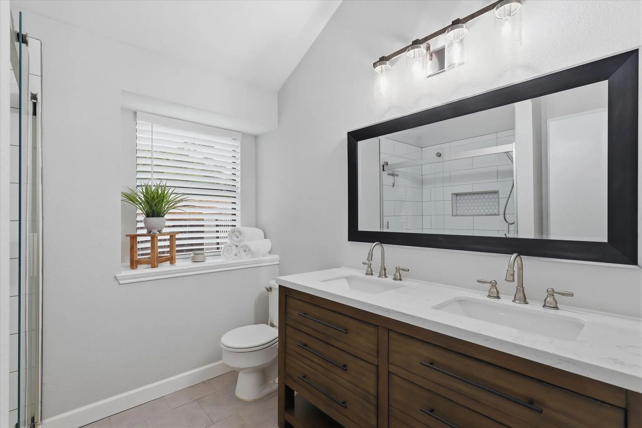 Beautifully updated primary bath features a dual-sink vanity with quartz countertop and an oversized mirror.