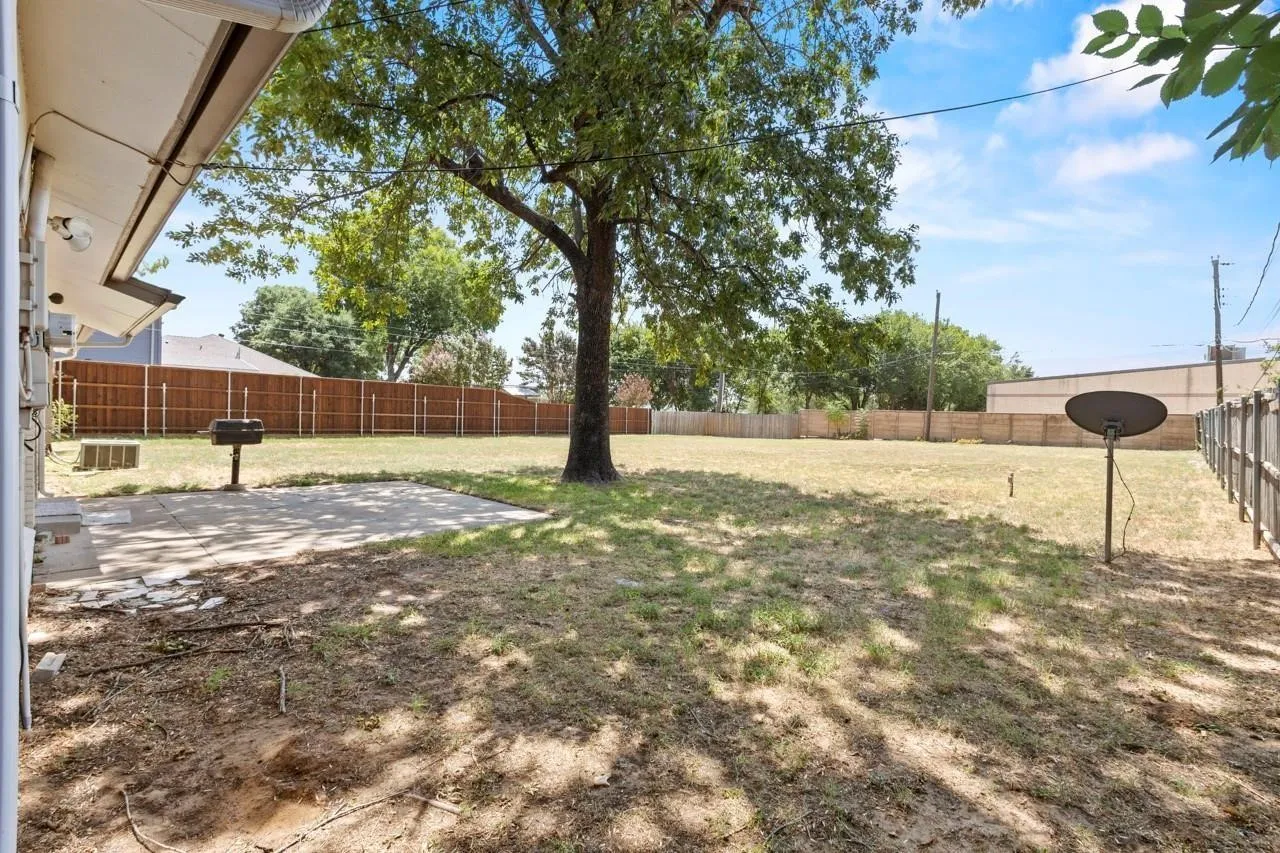 Expansive backyard featuring a mature tree, concrete patio, and perimeter fencing