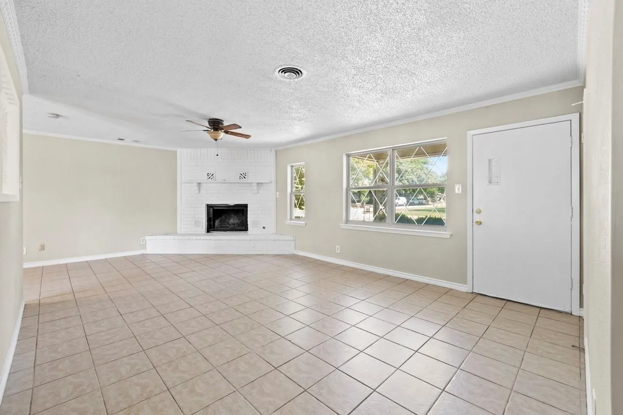 Spacious room with tile flooring, featuring a white brick fireplace, ceiling fan, and multiple windows