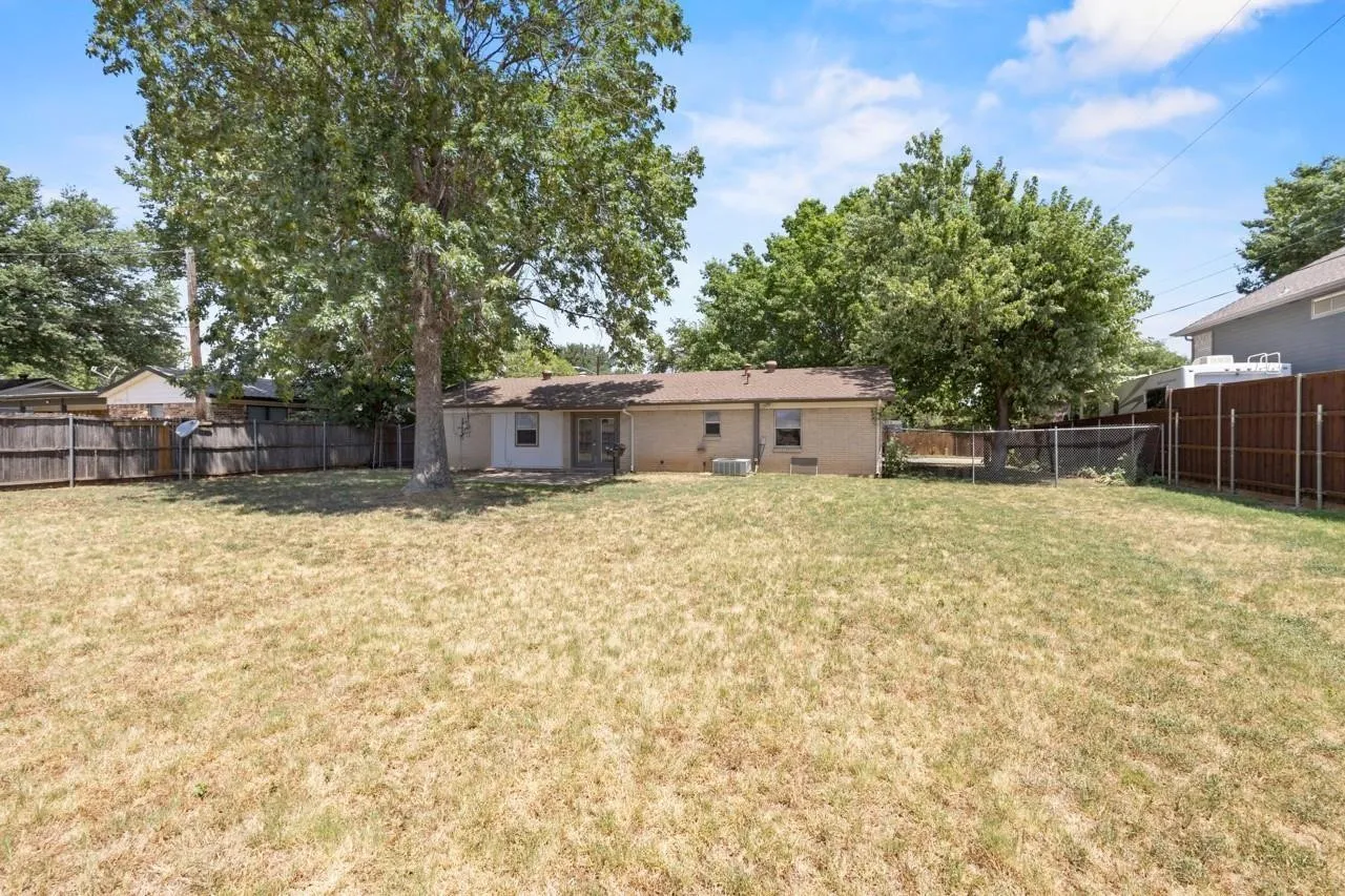 Expansive backyard featuring a large mature tree, wood fencing, and a brick exterior