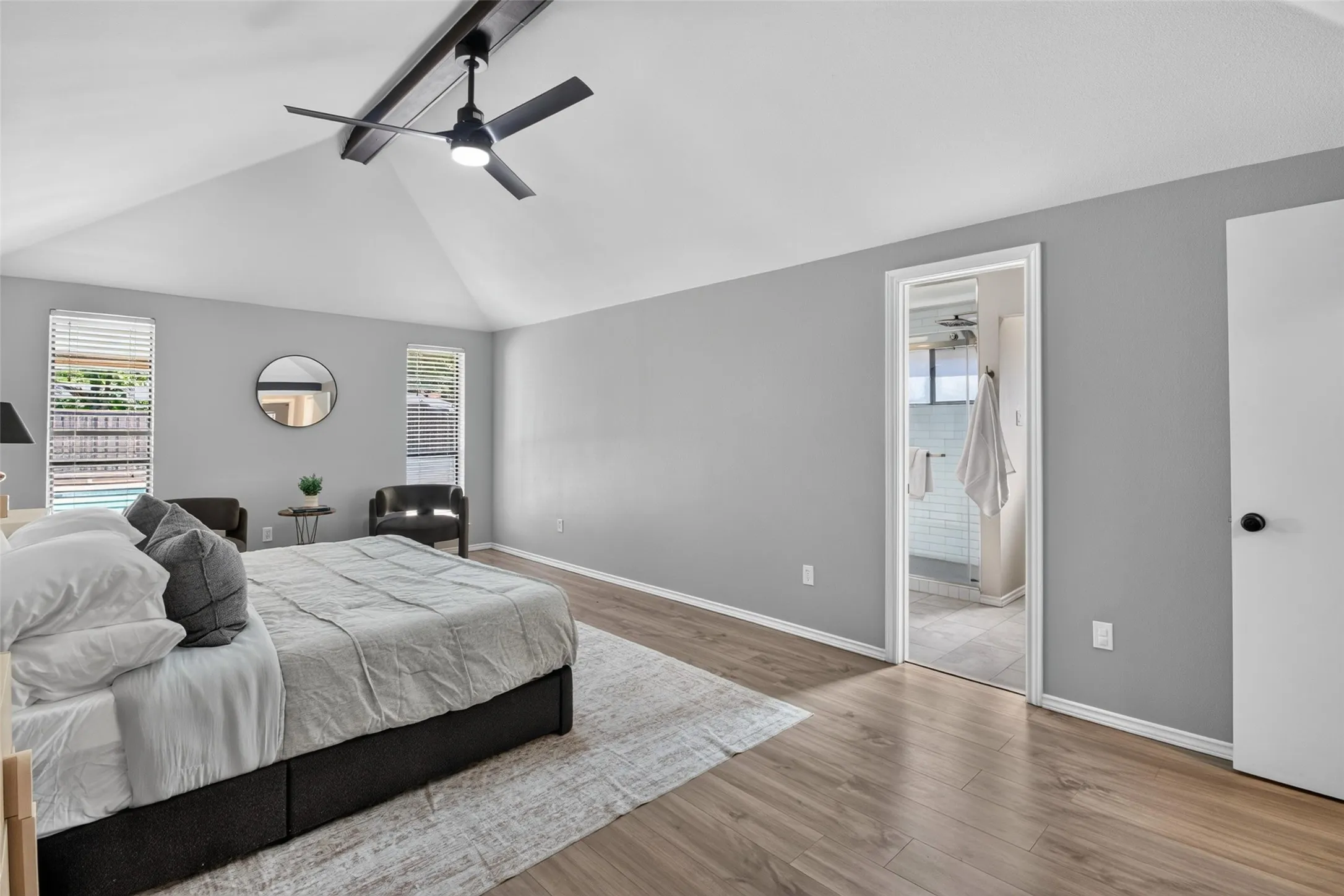 Vaulted ceiling with exposed beam, ceiling fan, wood-finish flooring, and a bathroom entrance with tiled flooring