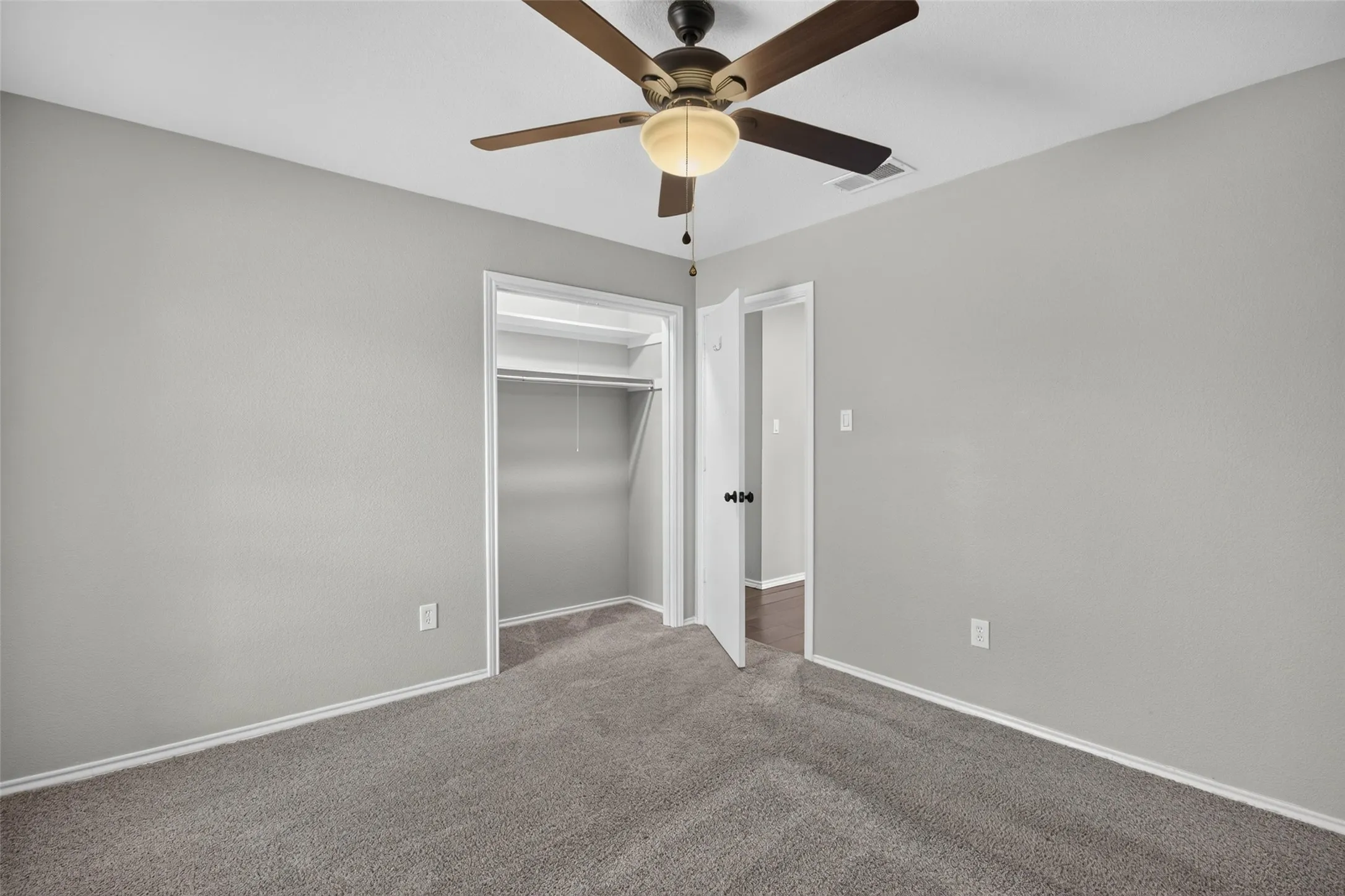 Neutral tone walls, ceiling fan with integrated lighting, gray carpeting, and a built-in closet with shelving