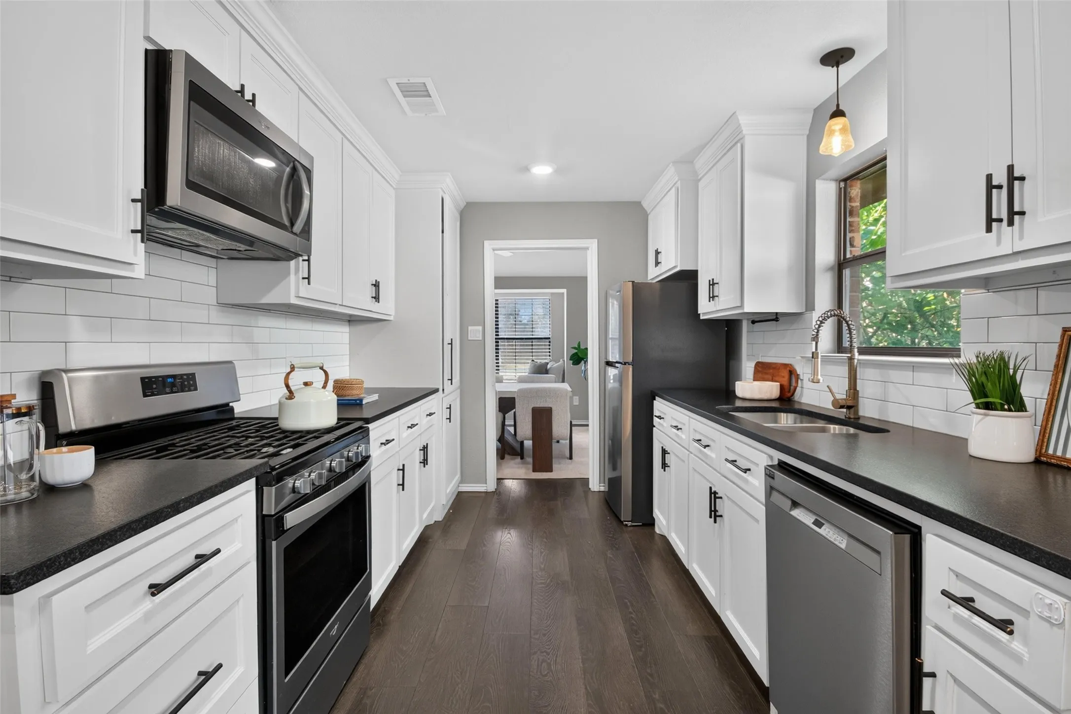White cabinetry with matte black hardware, stainless steel appliances, dark wood-finish flooring, subway tile backsplash, and dark countertops