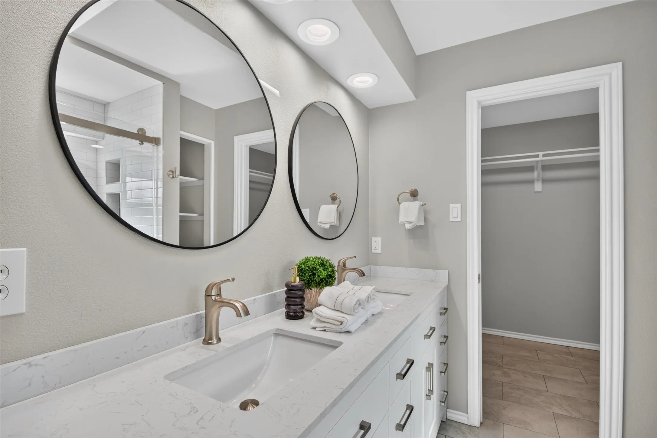Dual vanity with integrated sinks, brushed bronze fixtures, and round black-framed mirrors