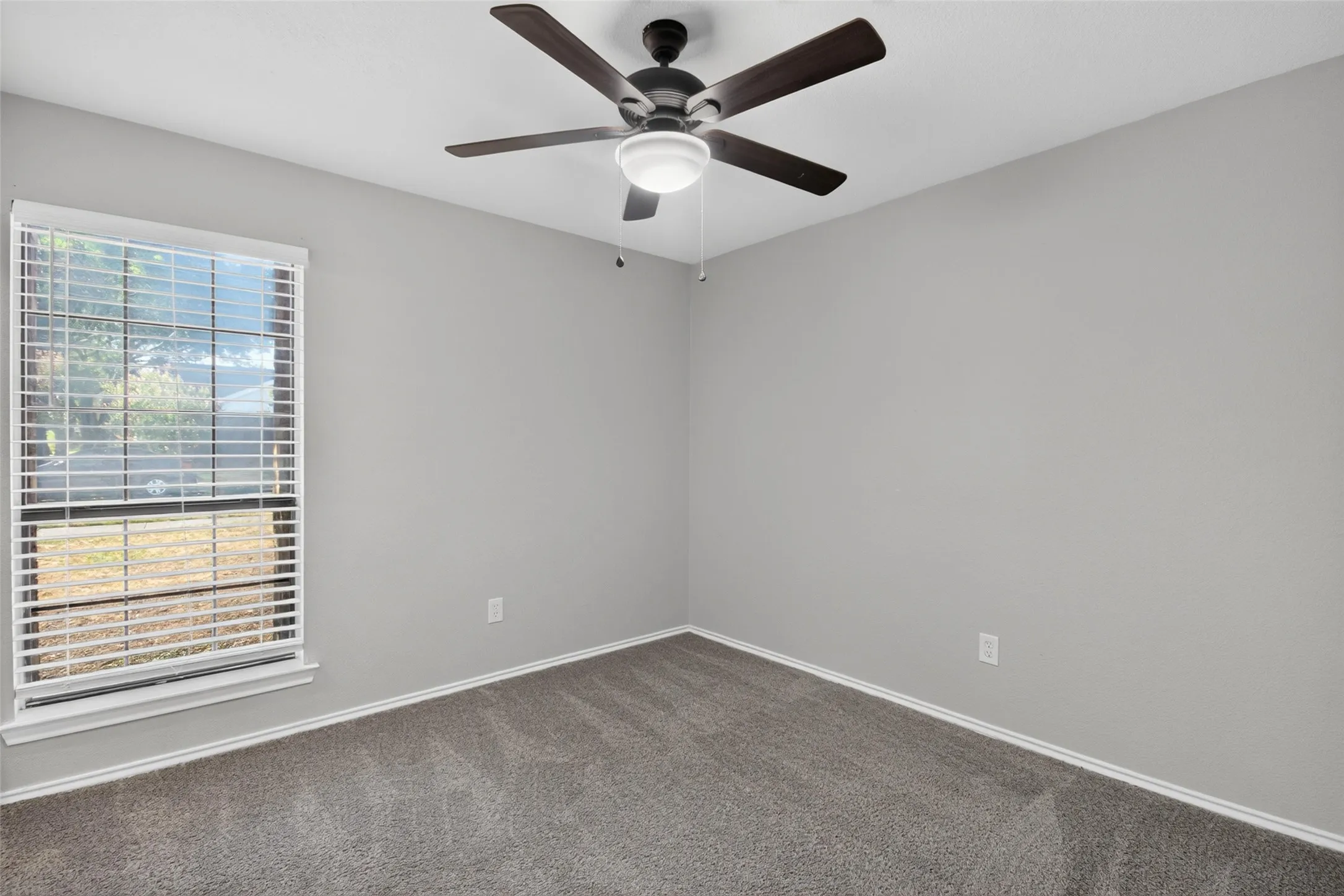 Neutral gray walls, dark gray carpet, white window trim, horizontal blinds, and a ceiling fan with integrated lighting