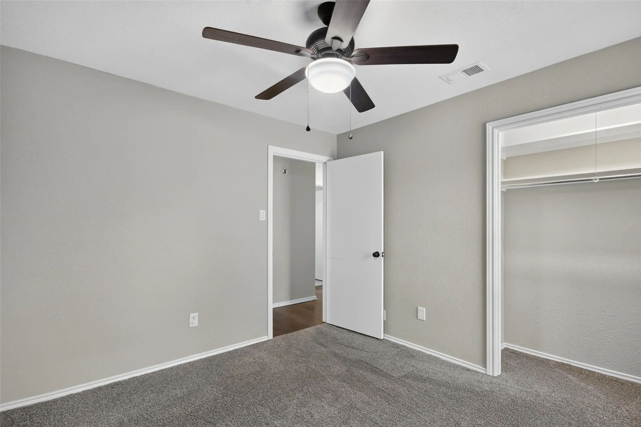 Plush grey carpet flooring, light grey painted walls, ceiling fan with integrated lighting, and a closet with a built-in hanging rod