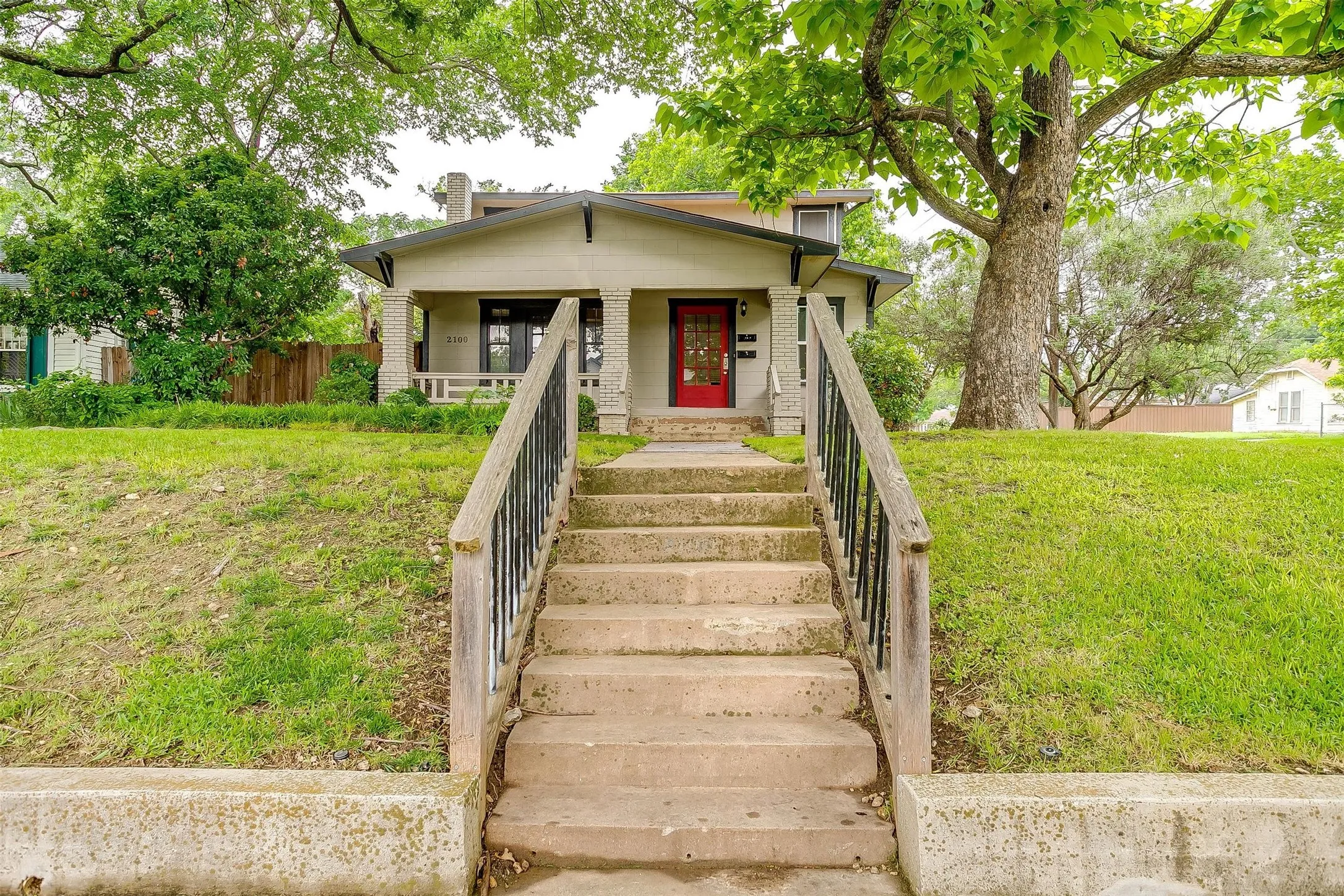 Welcoming front elevation featuring a covered entry porch with metal railings, concrete steps with side walls, and a red entry door