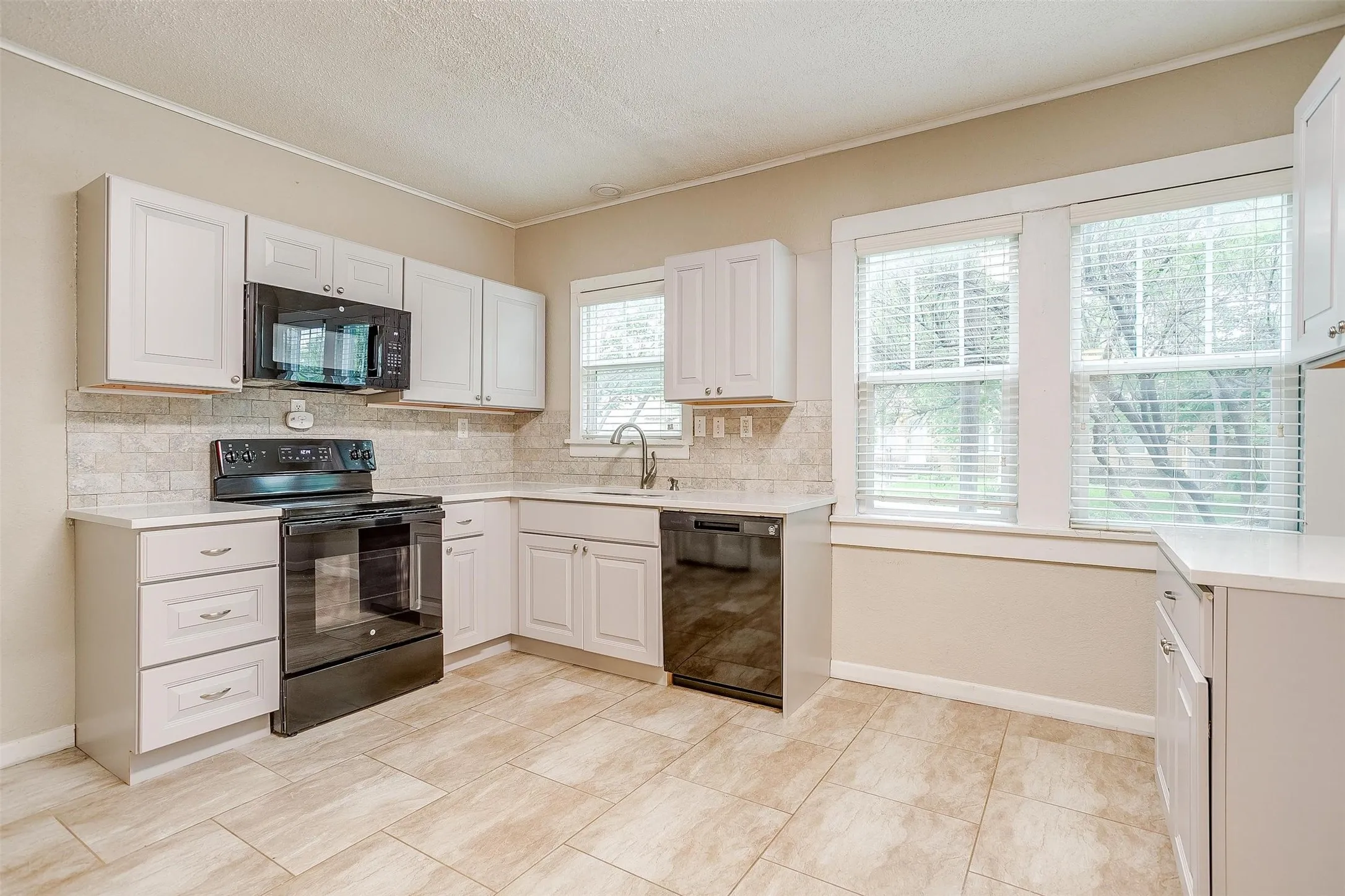 Bright, remodeled kitchen featuring white cabinetry, stainless steel appliances, tile backsplash, and ceramic tile flooring