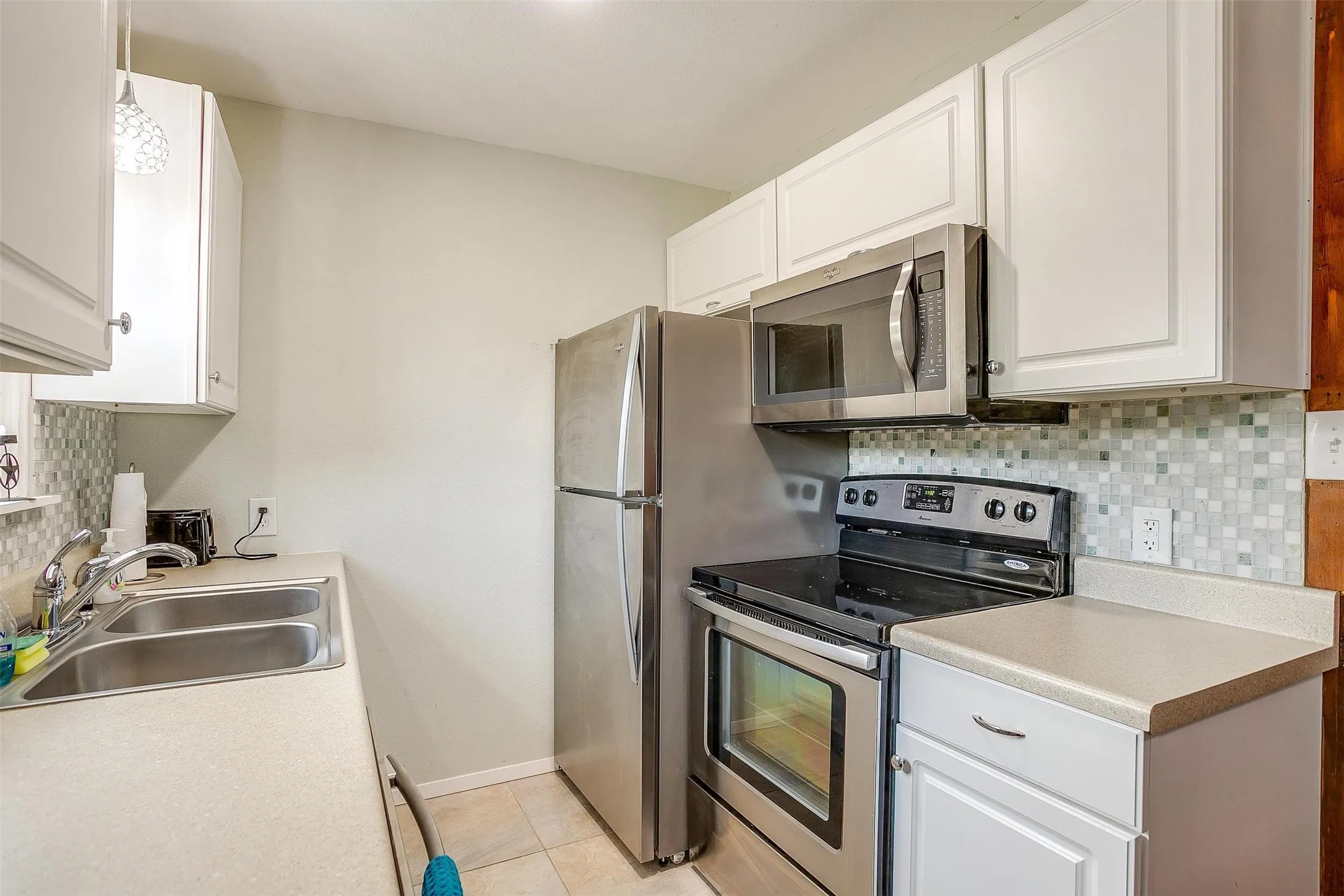 White cabinetry with stainless steel hardware and appliances., mosaic tile backsplash, double basin stainless steel sink, and stainless steel appliances
