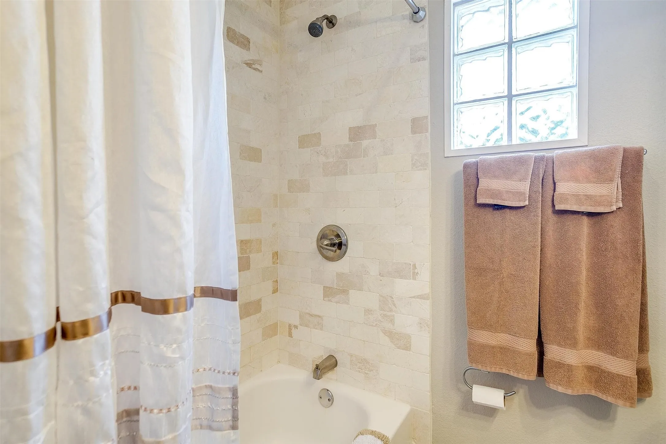 Bathtub and shower combination featuring tiled walls, a glass block window, and brushed nickel fixtures
