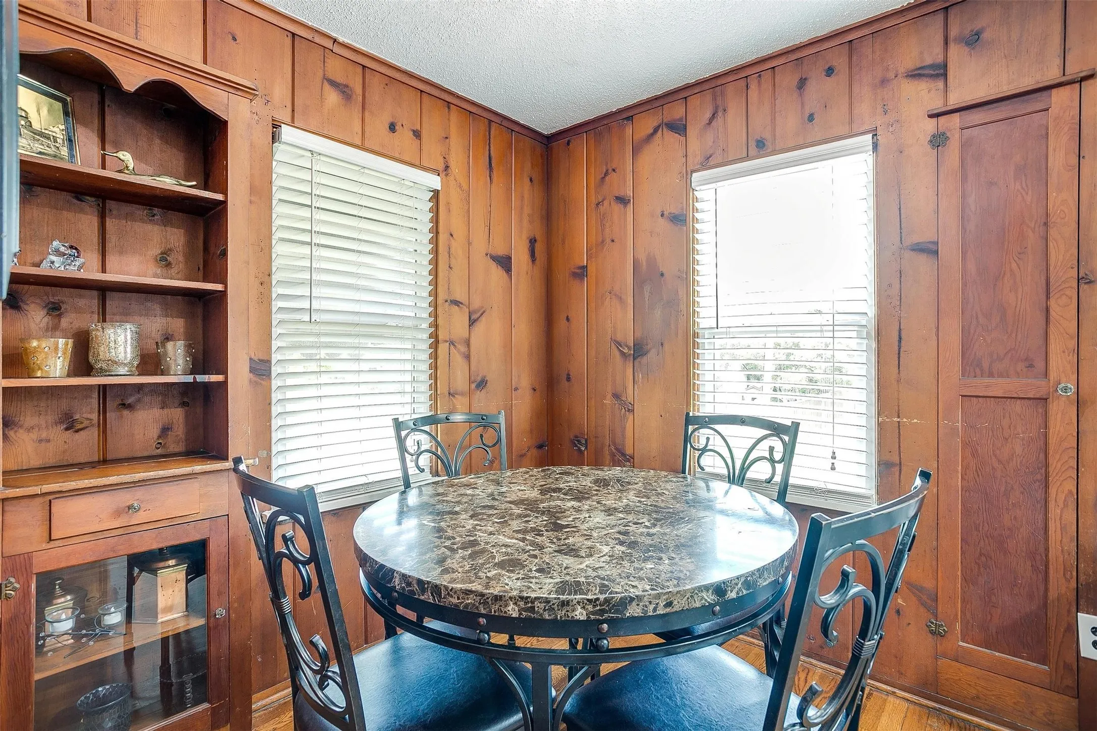 Wood-paneled walls with built-in wooden shelving, a built-in china cabinet with glass-front doors, and two windows