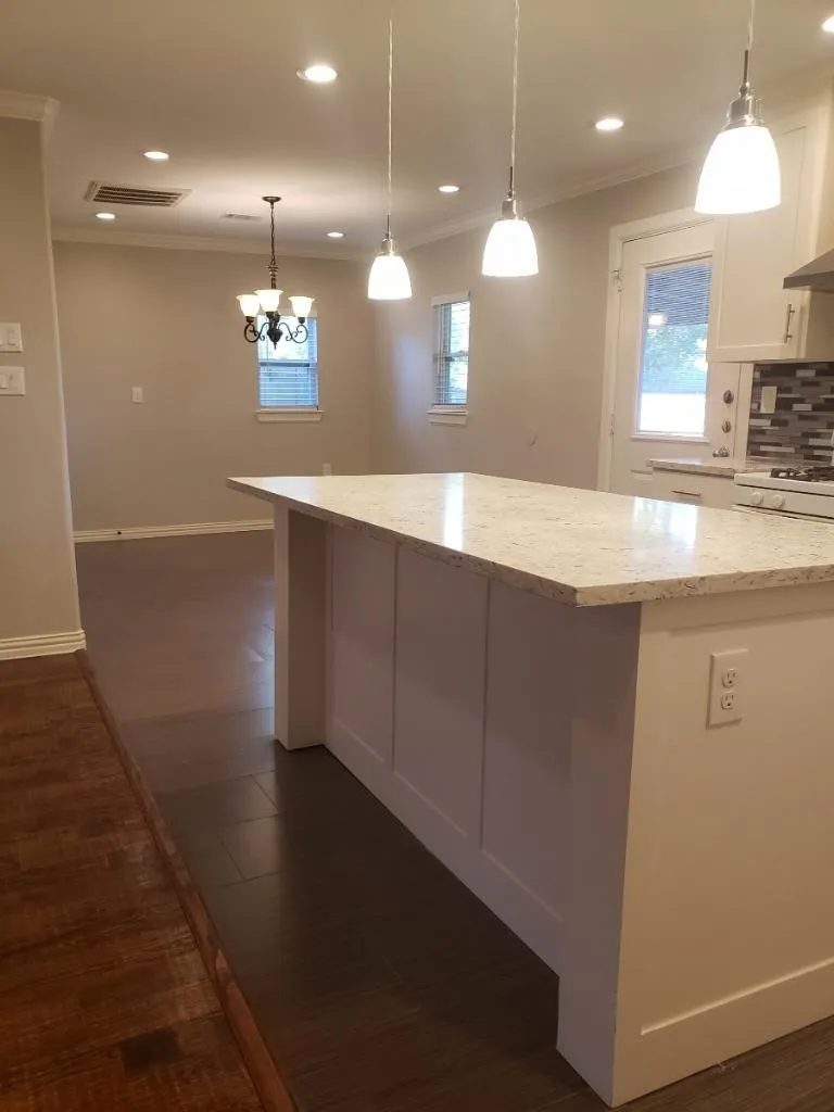 Modern kitchen featuring a substantial island with a light stone countertop, pendant lighting with frosted glass shades, recessed ceiling lights, and stainless steel​​‌​​​​‌​​‌‌​‌‌​​​‌‌​‌​‌​‌​​​‌​​ appliances