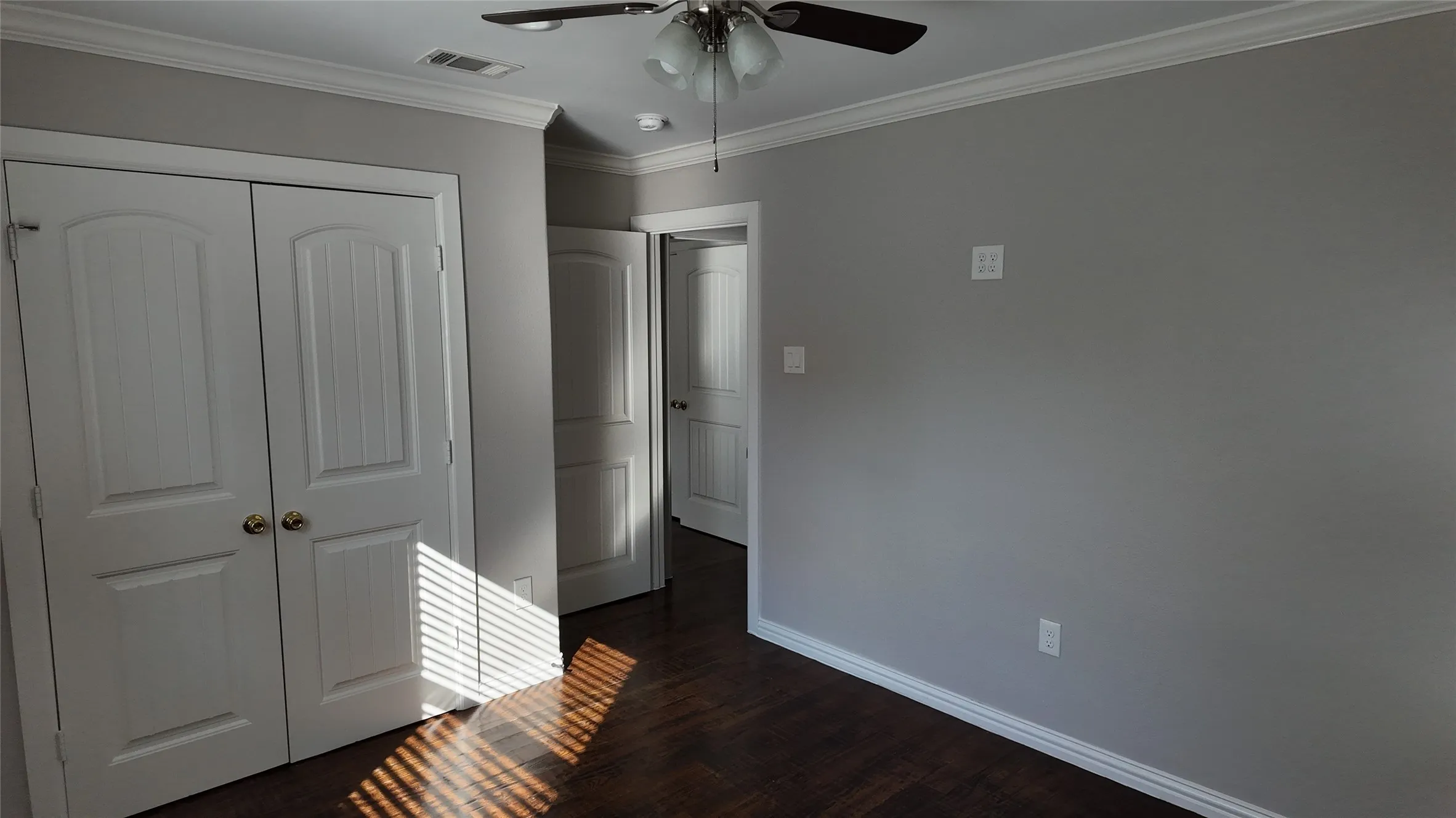 Wood-finish flooring, white crown molding, and a ceiling fan