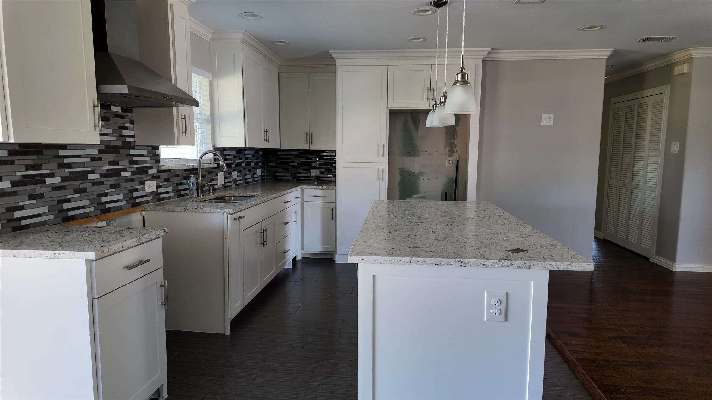 Kitchen featuring white cabinetry, light-toned countertops, a mosaic tile backsplash, a stainless steel range hood, and dark wood-finish flooring