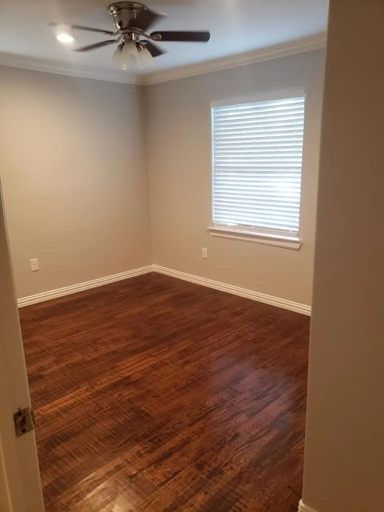 Wood-finish flooring, crown molding, ceiling fan with integrated lighting, and a window with blinds