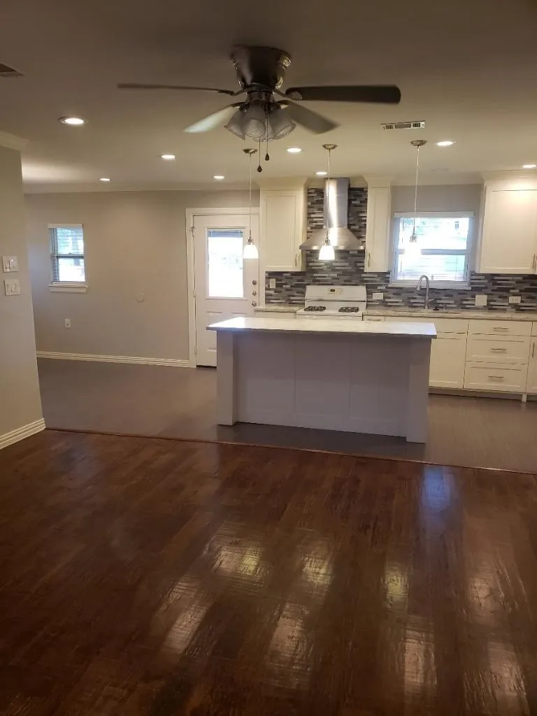 Open-concept kitchen and living area featuring warm wood-finish flooring, recessed ceiling lighting, and a ceiling fan