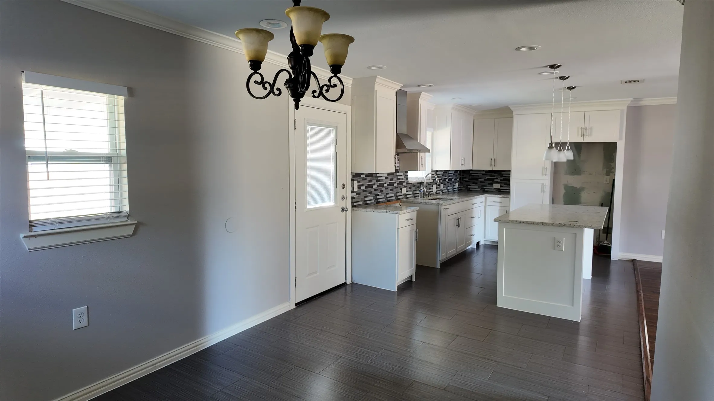 Open-concept kitchen and dining area featuring wood-finish flooring, white cabinetry, granite countertops, and a mosaic tile backsplash