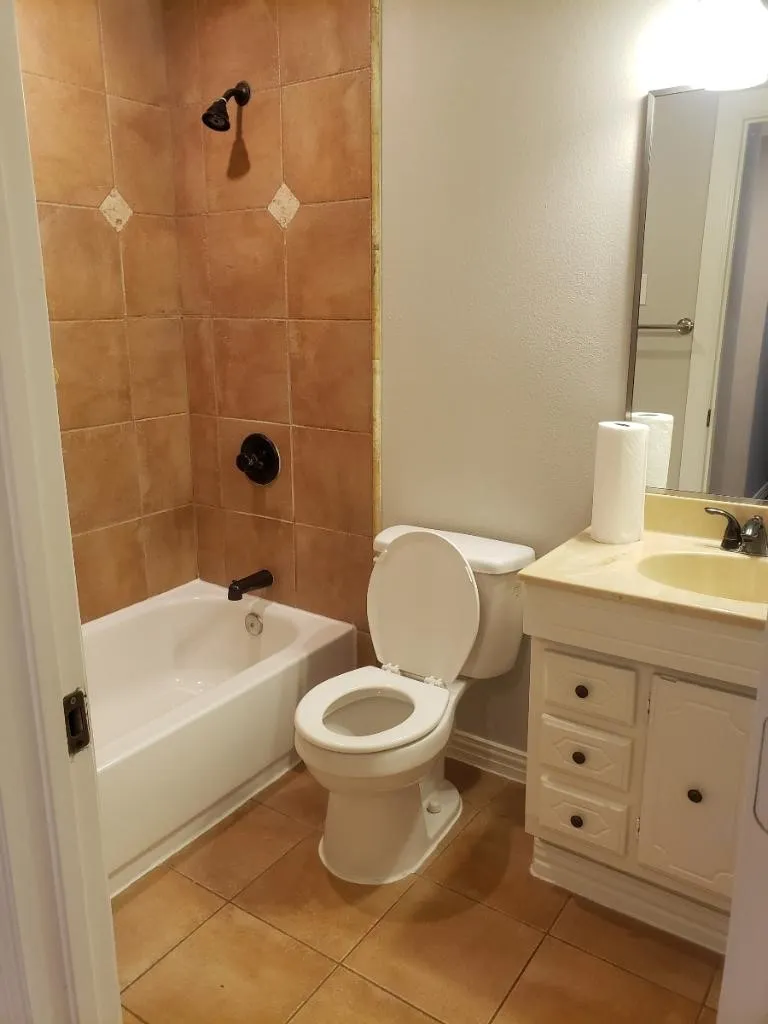 Bathroom featuring a tile-surround shower with dark bronze fixtures, a white bathtub, a toilet, and a vanity with an integrated sink