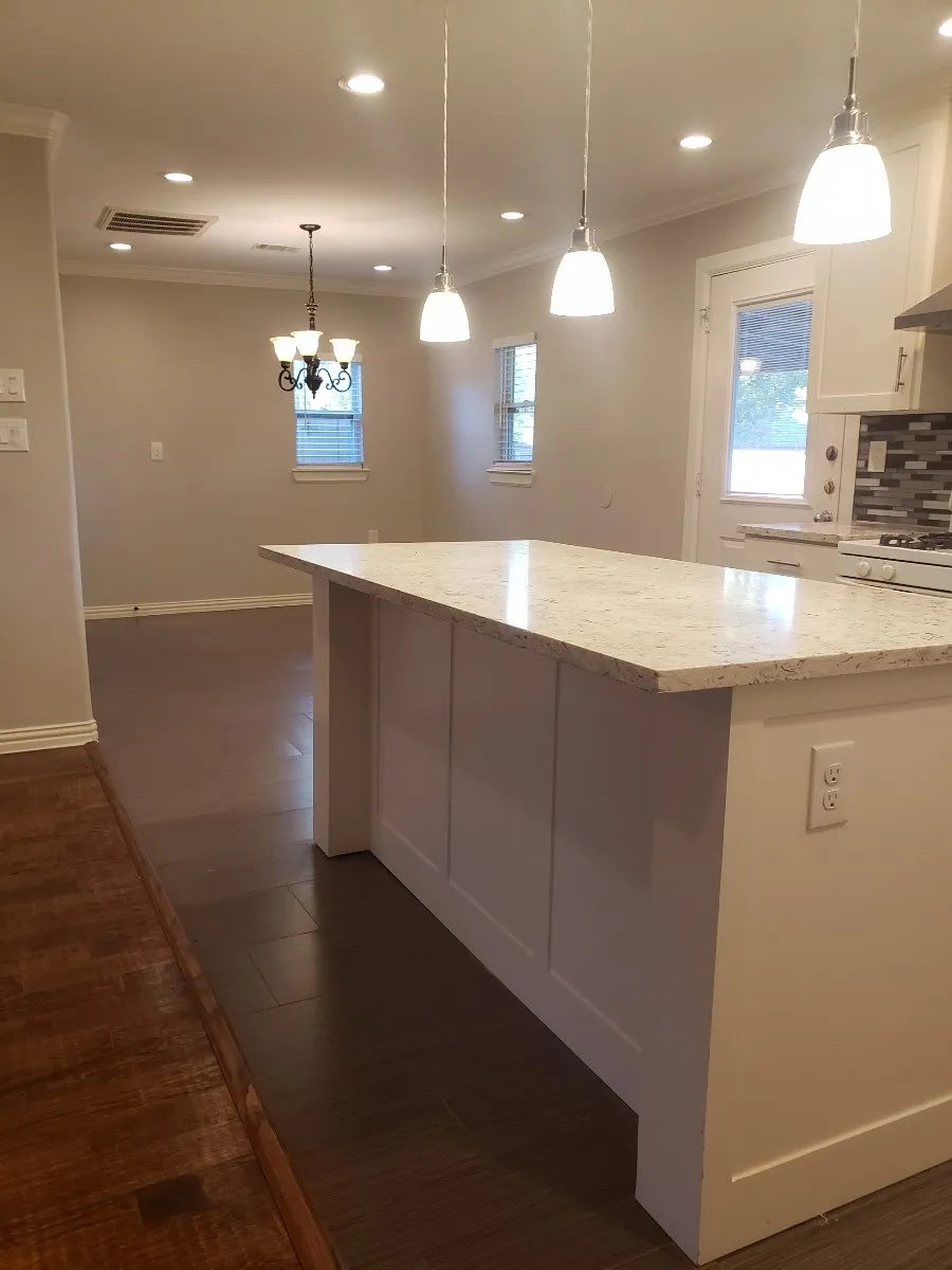 Kitchen island with a light-toned countertop, pendant lighting, built-in cabinetry, and wood-finish flooring