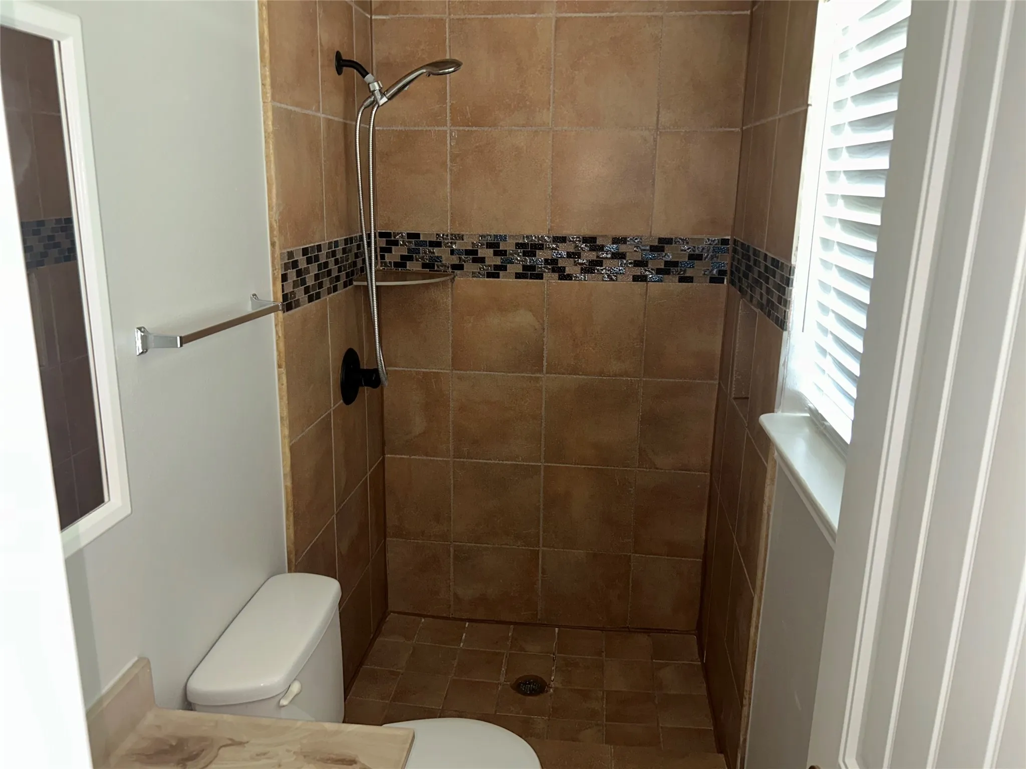 Tiled shower stall featuring a decorative mosaic accent band, built-in shelf, and handheld shower fixture