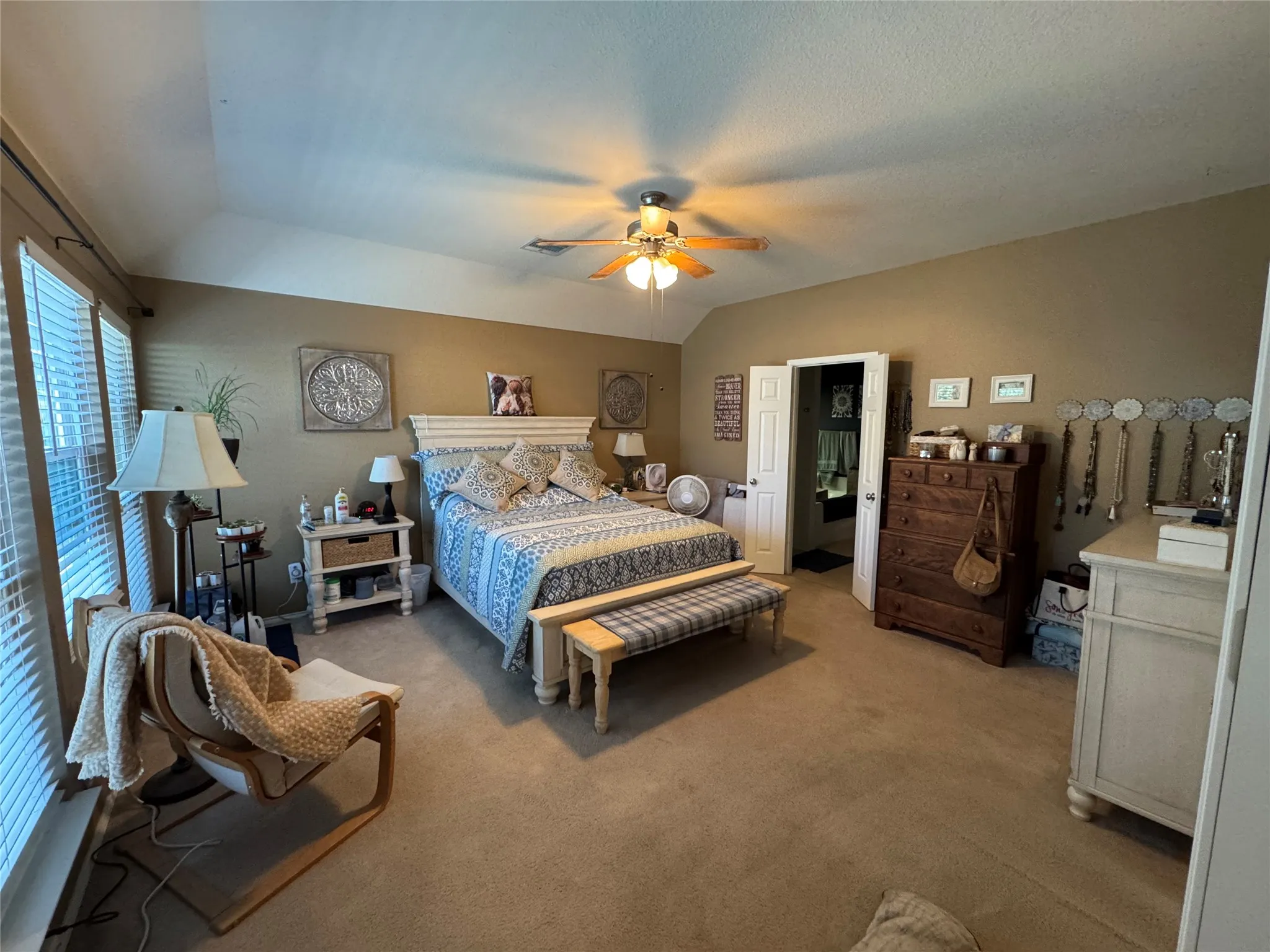 Carpeted bedroom with a vaulted ceiling, ceiling fan, and multiple windows with horizontal blinds