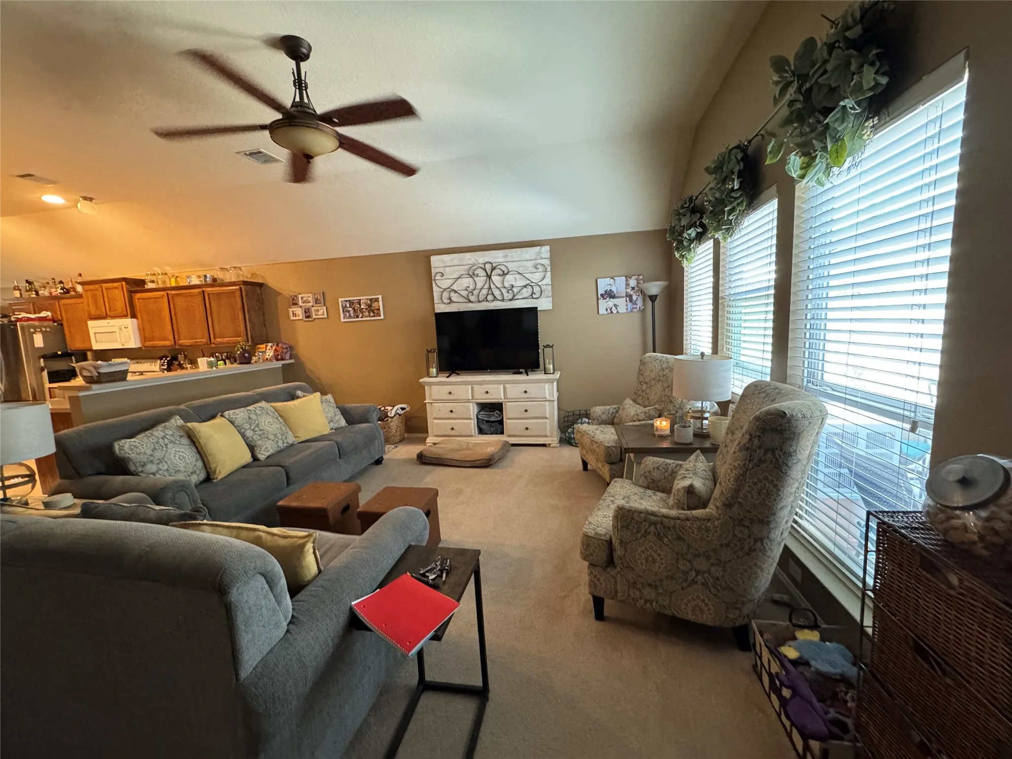 Spacious interior featuring a vaulted ceiling with a ceiling fan, multiple windows with blinds, a built-in kitchen counter, and wood-finish cabinetry