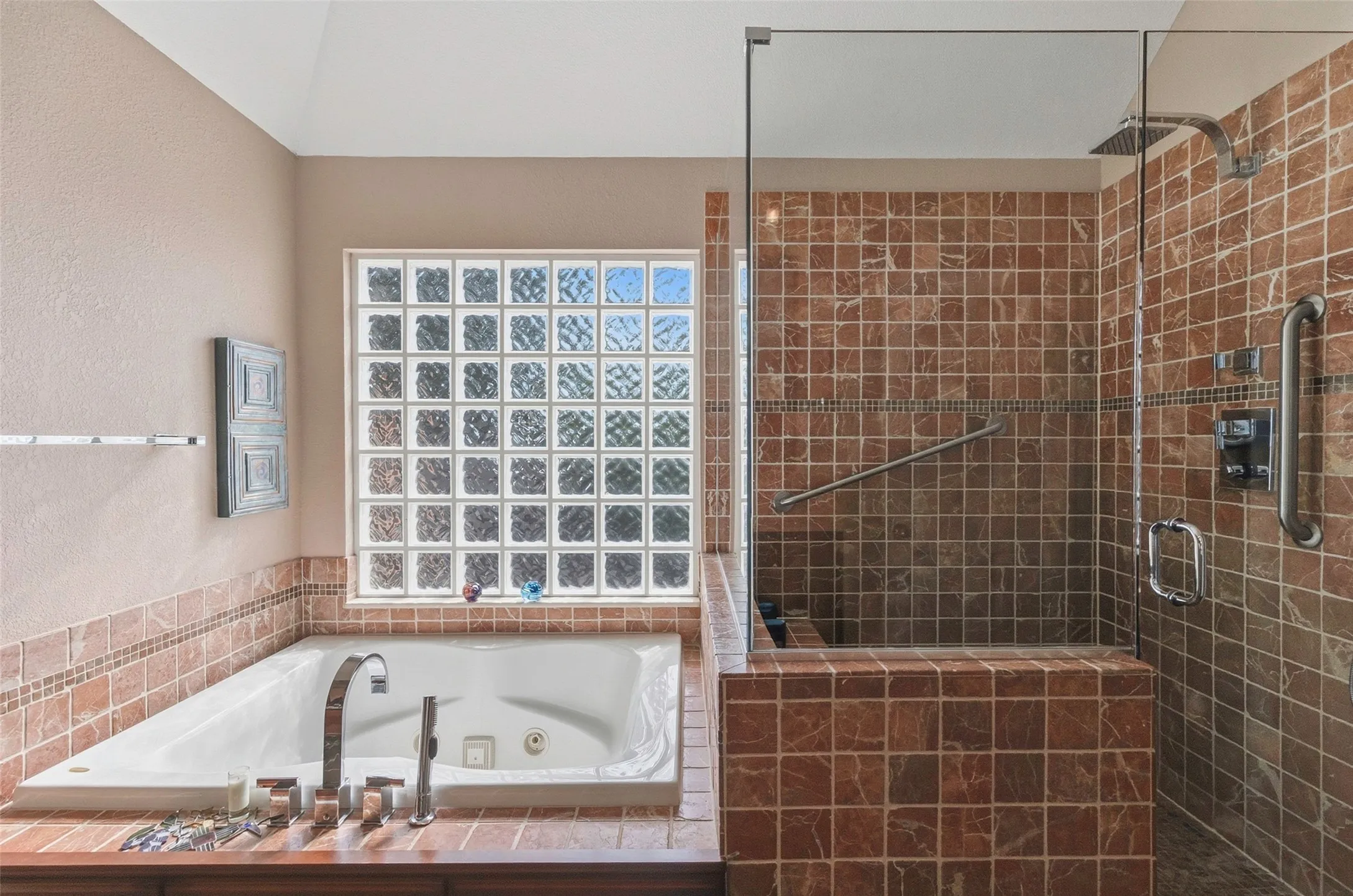 Soaking tub with deck-mounted fixtures, glass block window, and adjacent walk-in shower with glass enclosure and tiled walls