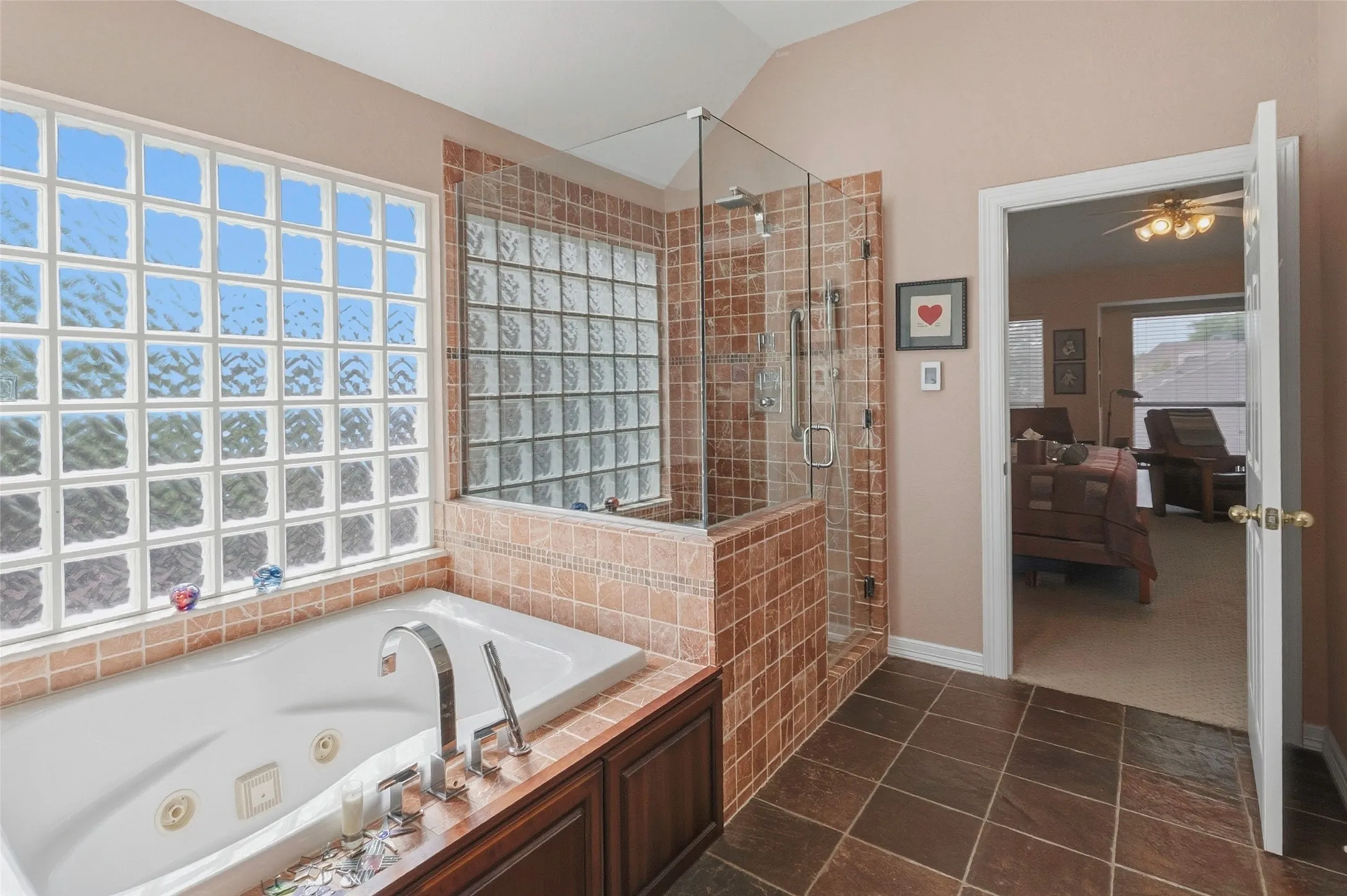 Soaking tub with chrome fixtures, glass block window, tile shower enclosure with glass door, dark wood-finish cabinetry, and brown tile flooring