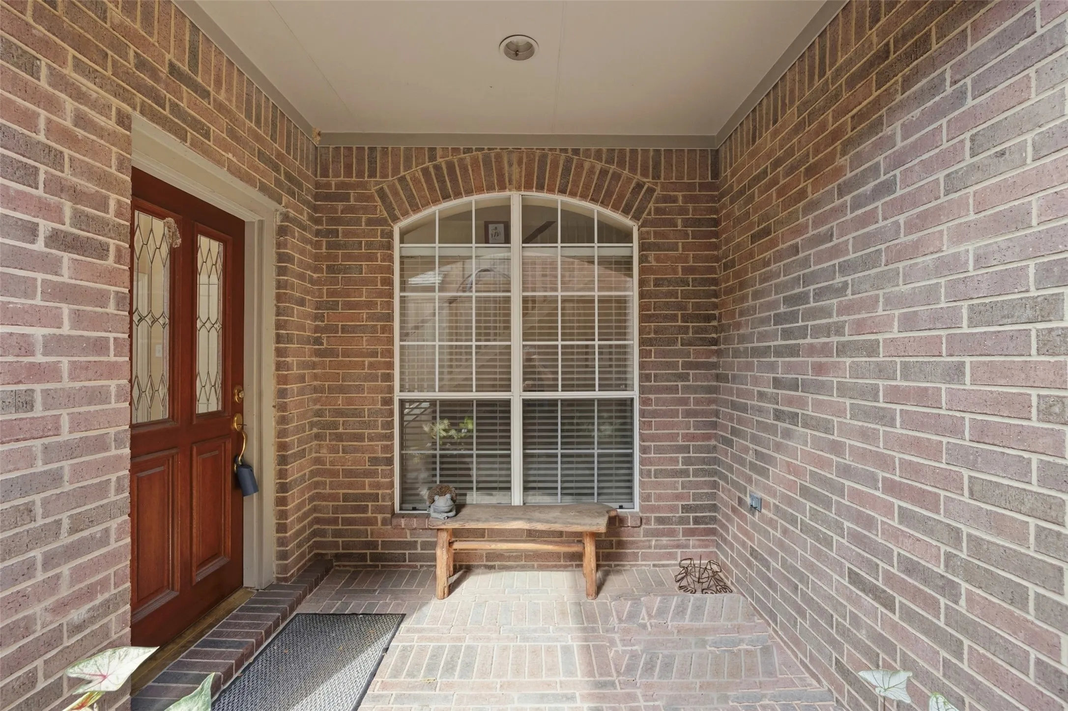 Brick exterior with an arched window, solid wood entry door with glass inserts, recessed lighting, and brick flooring