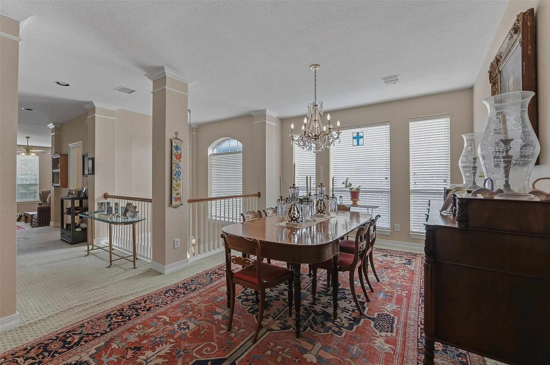 Elegant dining room featuring a crystal chandelier, formal dining table with seating for multiple guests, rich wood cabinetry, large arched transom windows with plantation shutters, and a decorative Persian-style area rug anchoring the space