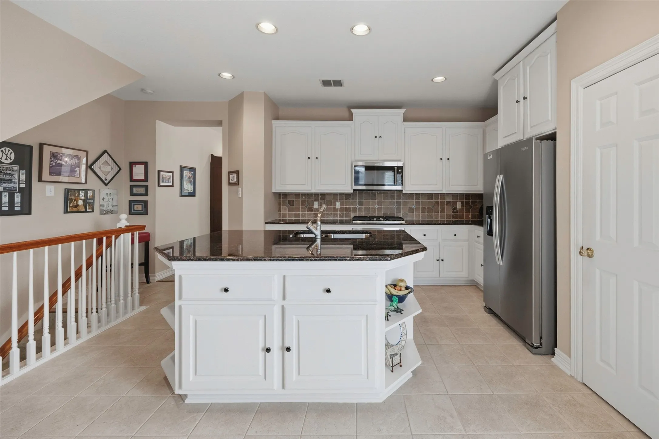 White cabinetry, dark stone countertops, stainless steel appliances, tiled backsplash, and recessed lighting