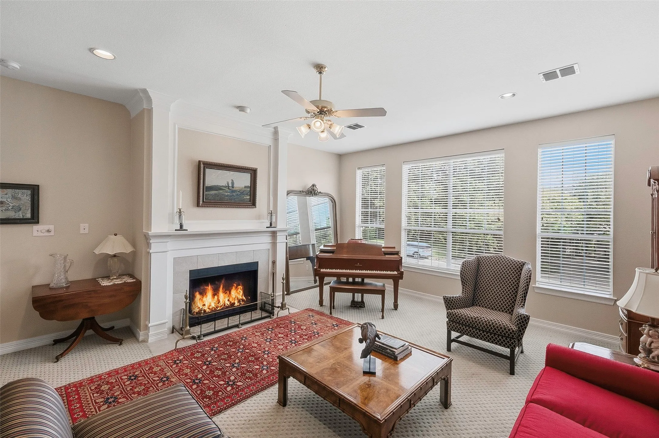 Fireplace with a tile surround and white mantel, recessed lighting, ceiling fan, and multiple windows
