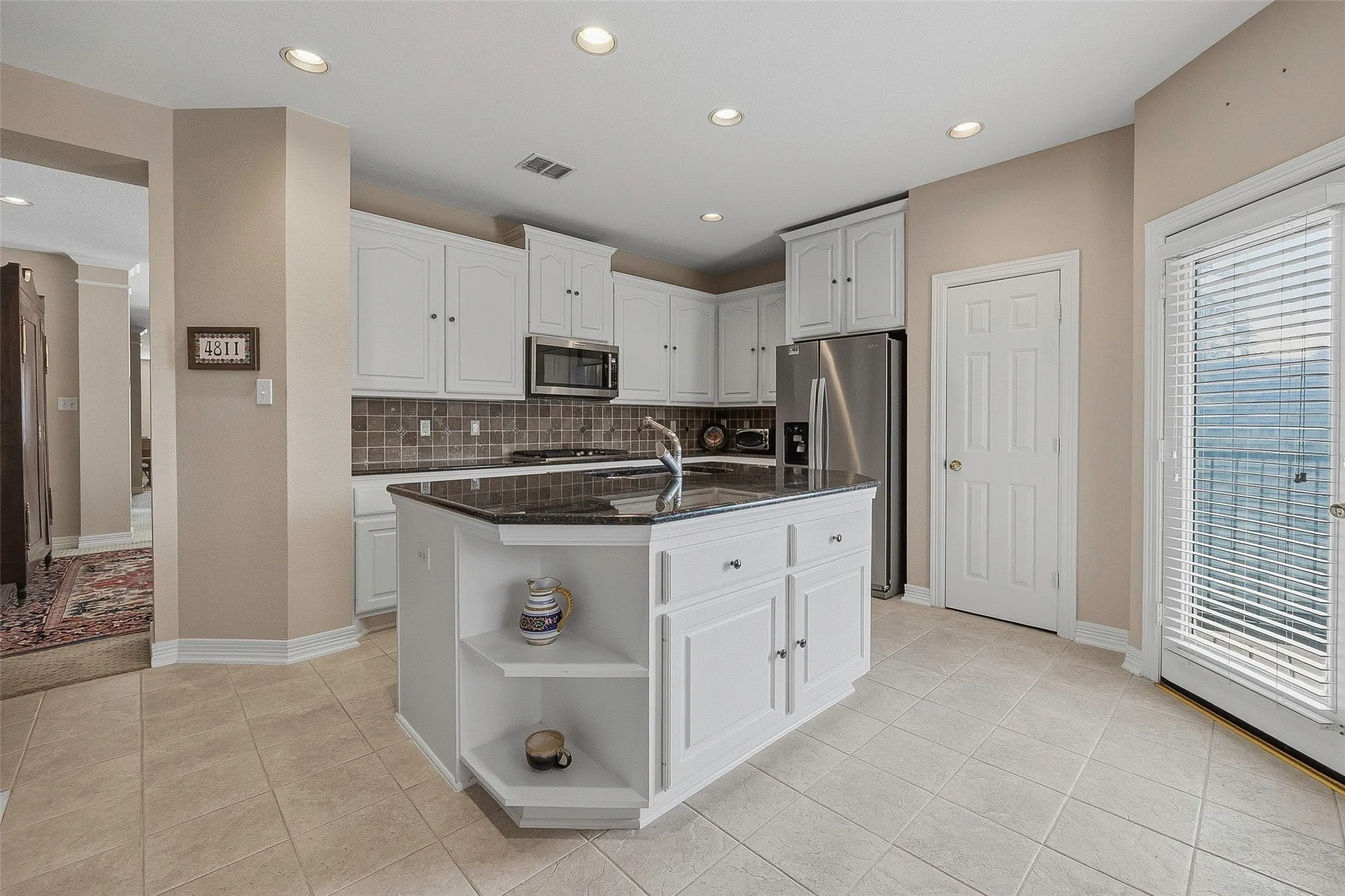 Kitchen featuring a central island with granite countertop, white cabinetry, integrated stainless steel appliances, and tile flooring