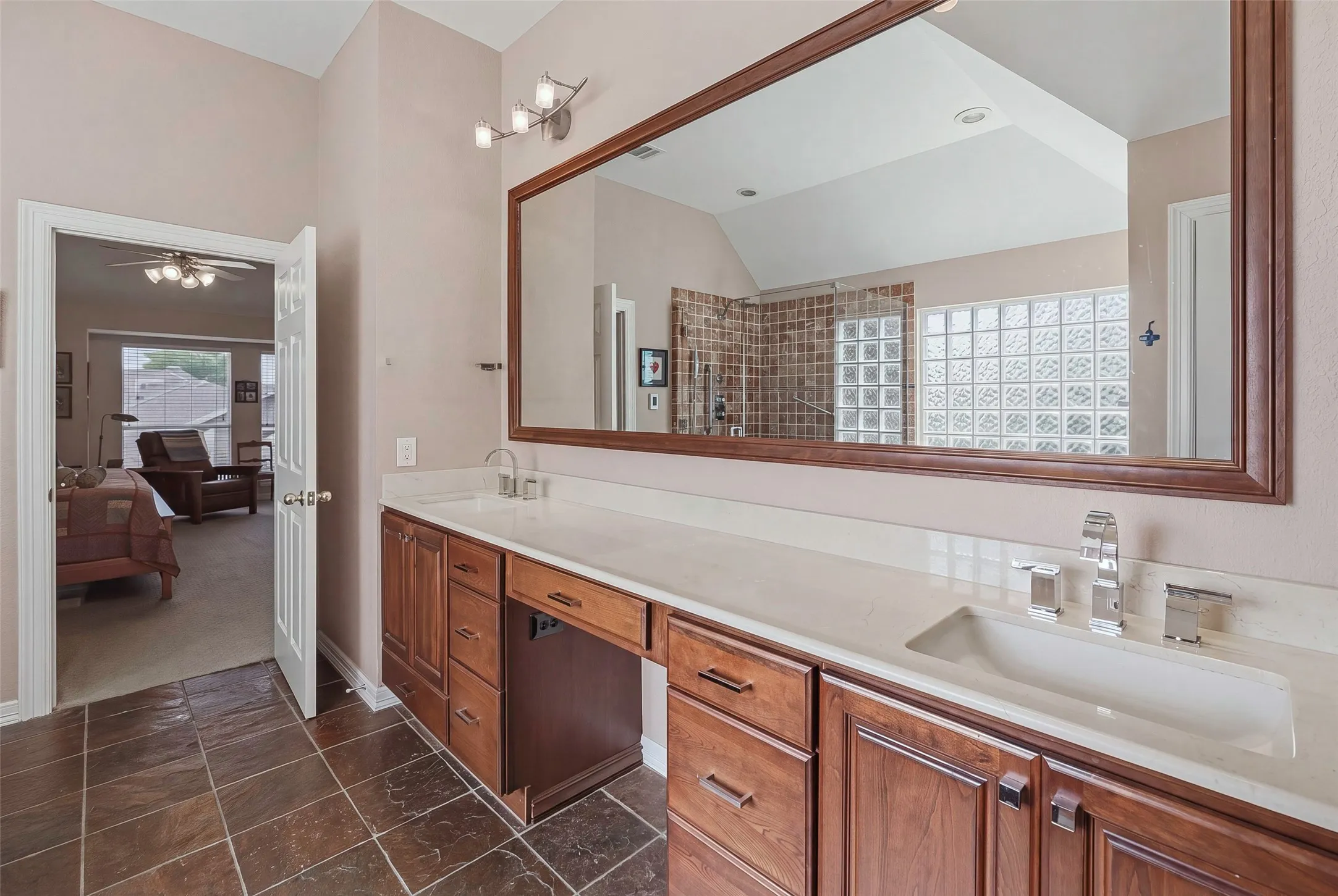 Dual vanity with integrated sinks, expansive framed mirror, wood cabinetry, and tiled flooring