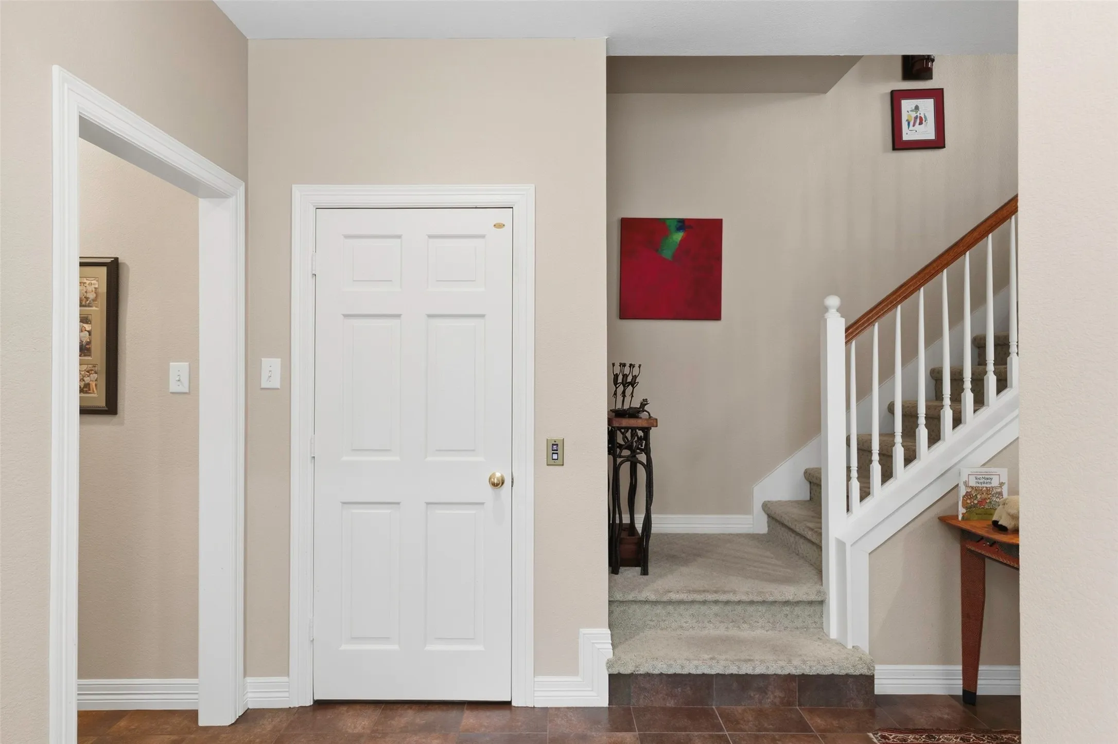 Six-panel interior door, wood-finish flooring, white painted baseboards, carpeted stairs, and a white balustrade with a wood handrail