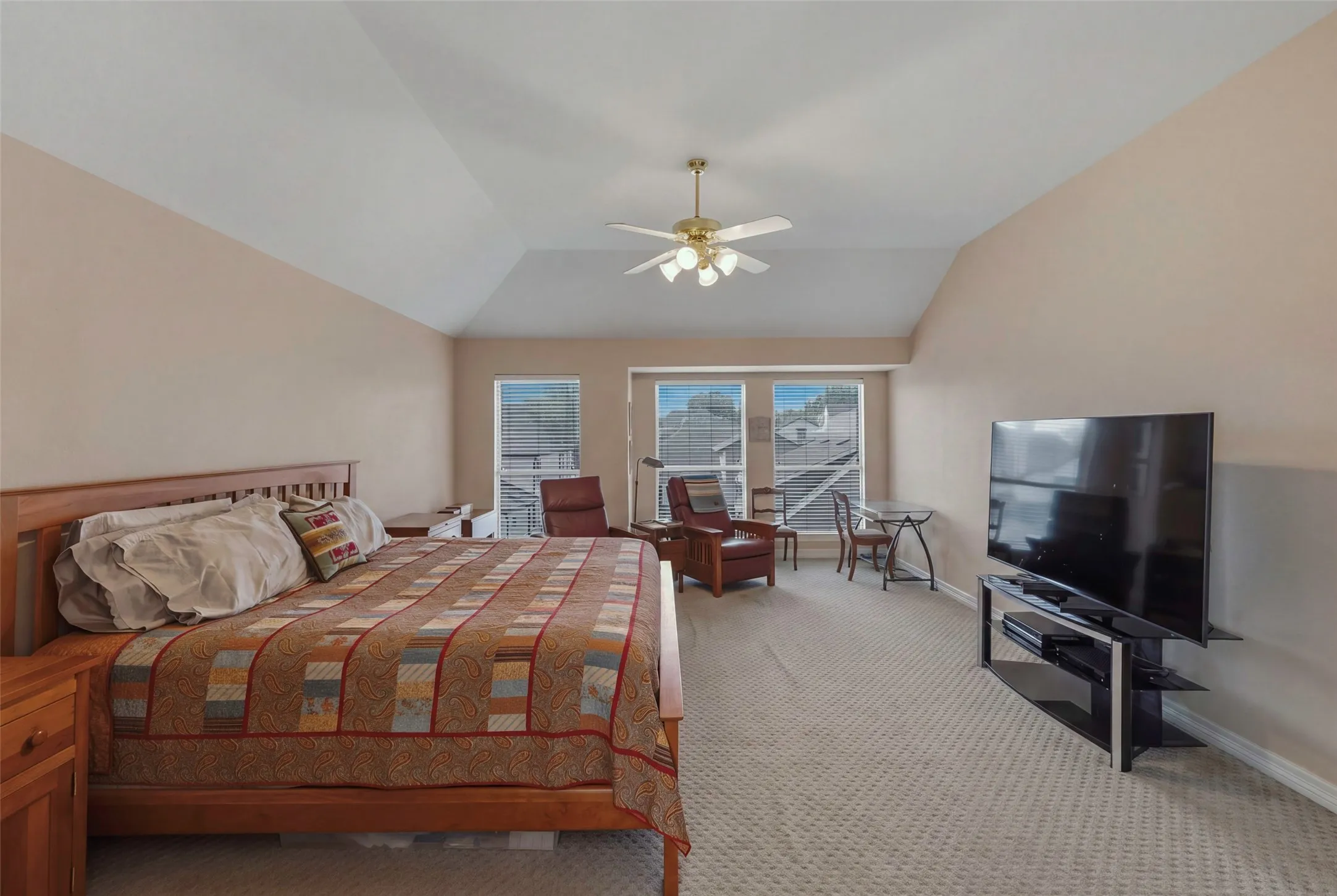 Vaulted ceiling with ceiling fan, three windows with blinds, carpeted flooring