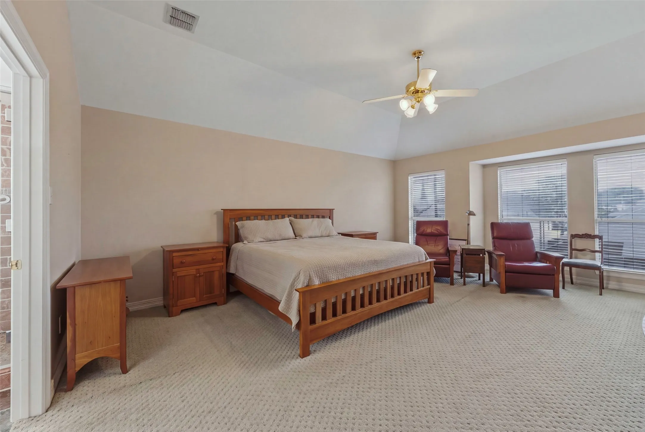 Tray ceiling with a ceiling fan, carpeting, multiple windows with blinds, and recessed bay window area