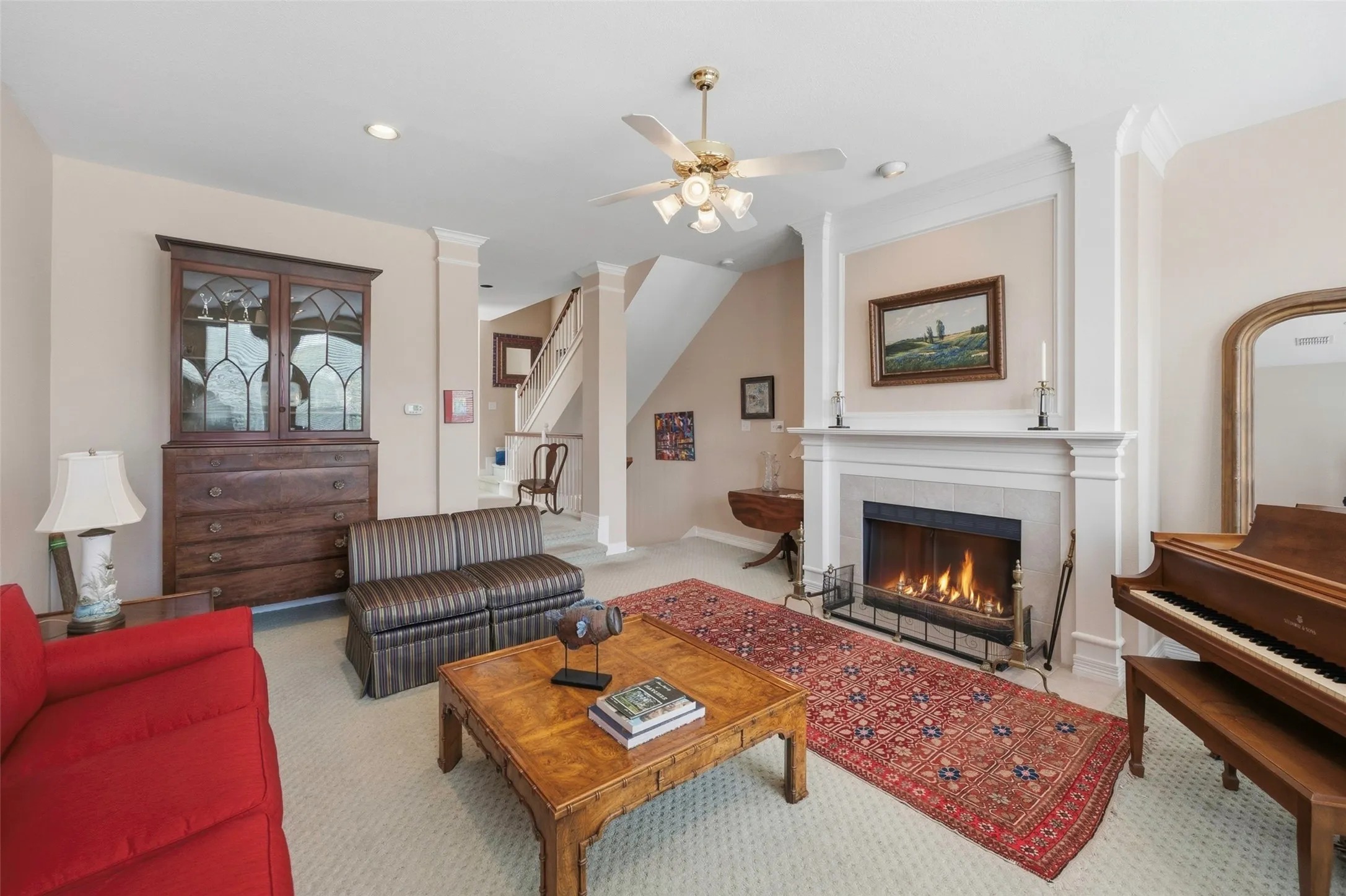 Recessed lighting, ceiling fan light fixture, built-in fireplace with a stone surround and mantle, and an open staircase with wood banister