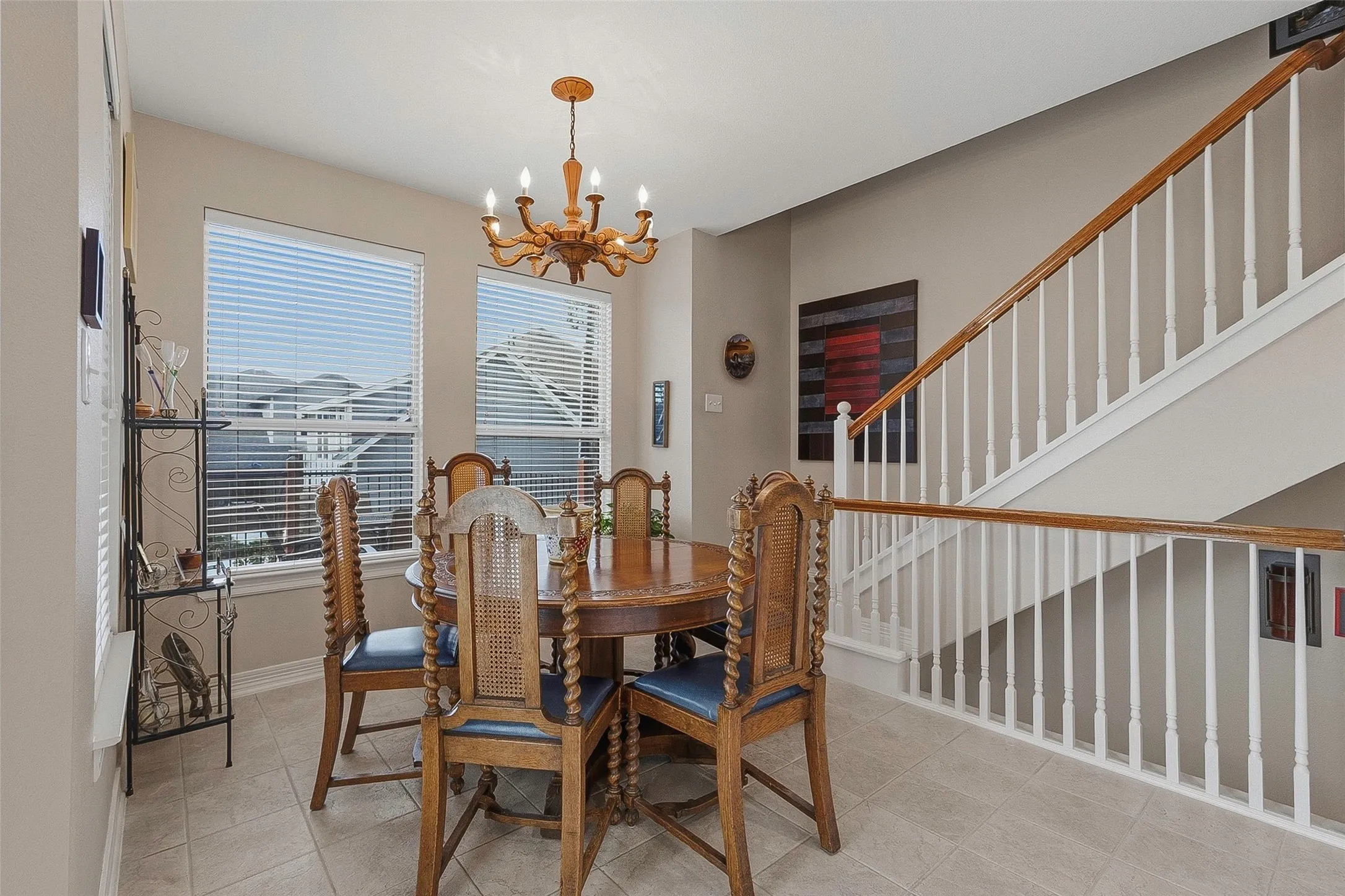 Neutral tone wall paint, two windows with blinds, wood chandelier, tiled flooring, and a staircase with wood handrails and white balusters