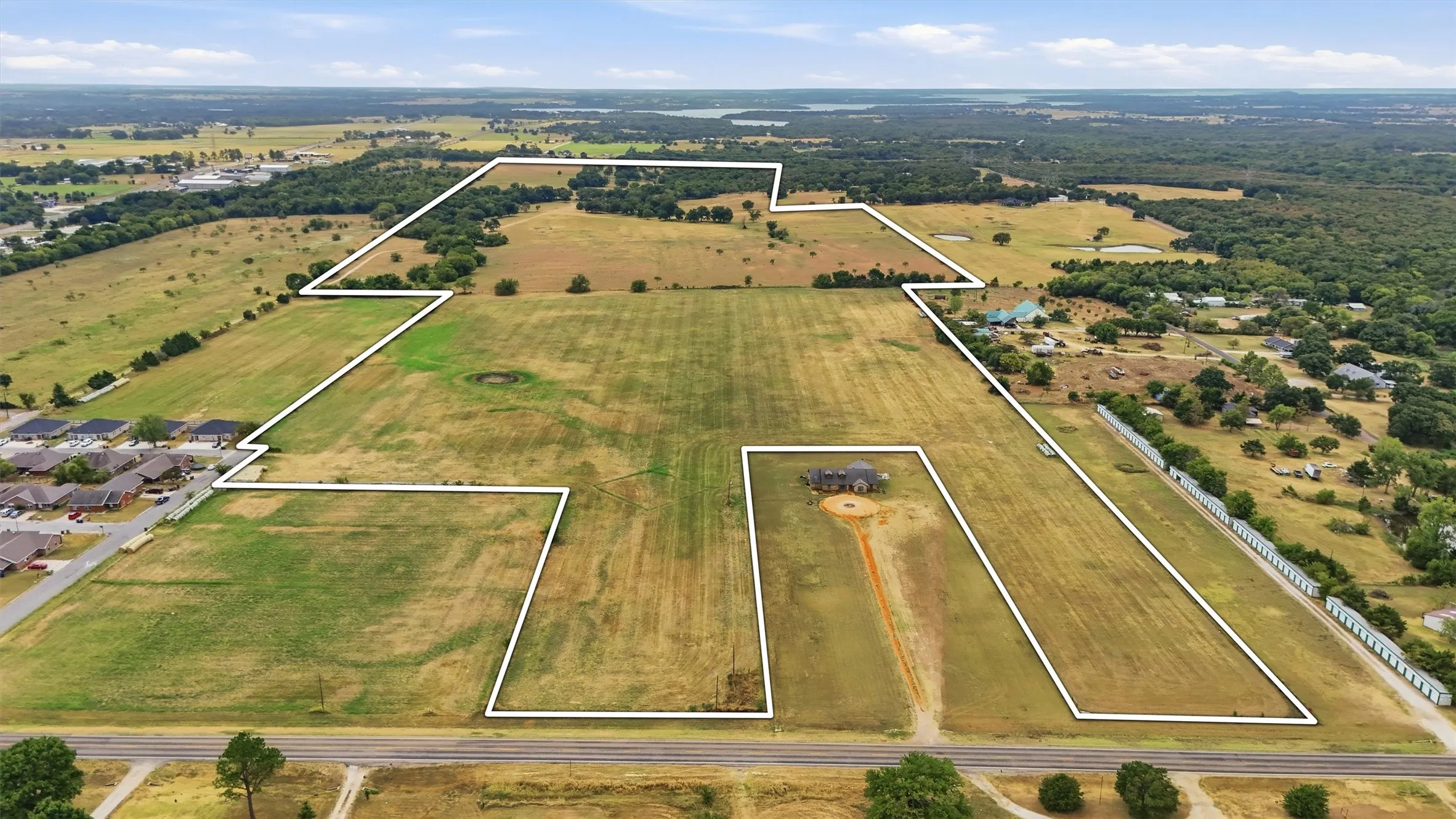 Expansive land parcel featuring open fields, scattered mature trees, and direct road frontage