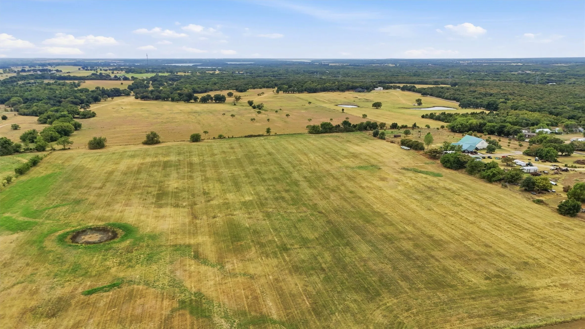 Expansive acreage featuring open fields, scattered mature trees, and a visible pond