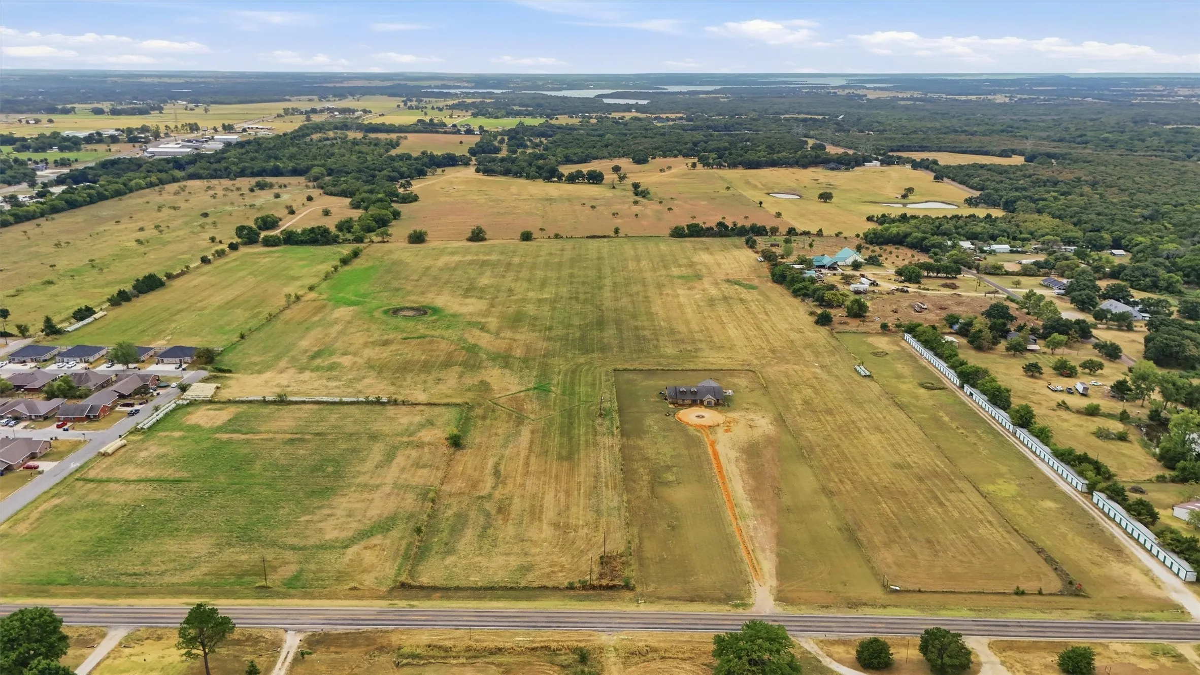 Expansive property featuring a large residence, surrounding green spaces, and a paved road frontage