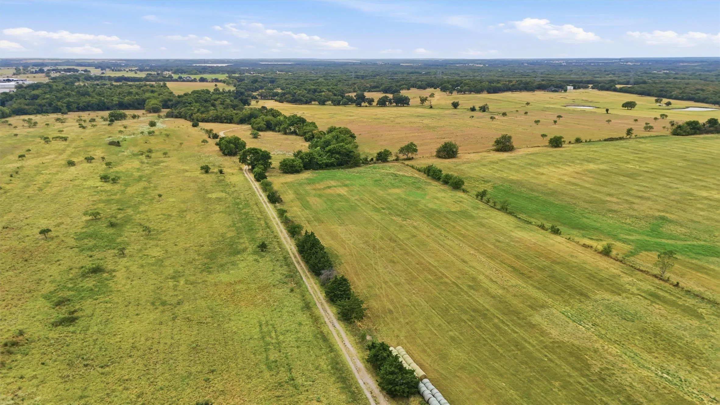 Expansive acreage with a gravel access road and multiple large fields