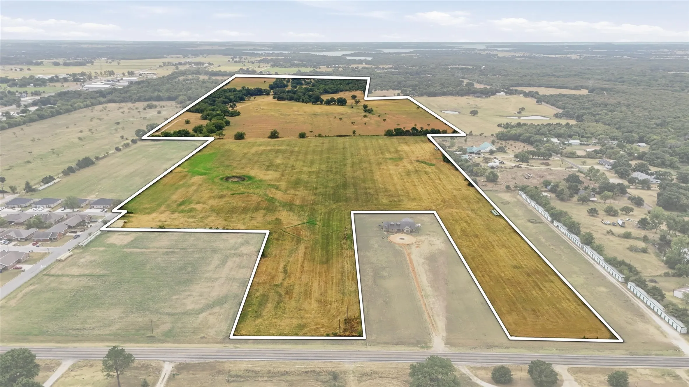 Expansive land parcel featuring open fields, scattered mature trees, and a visible road frontage