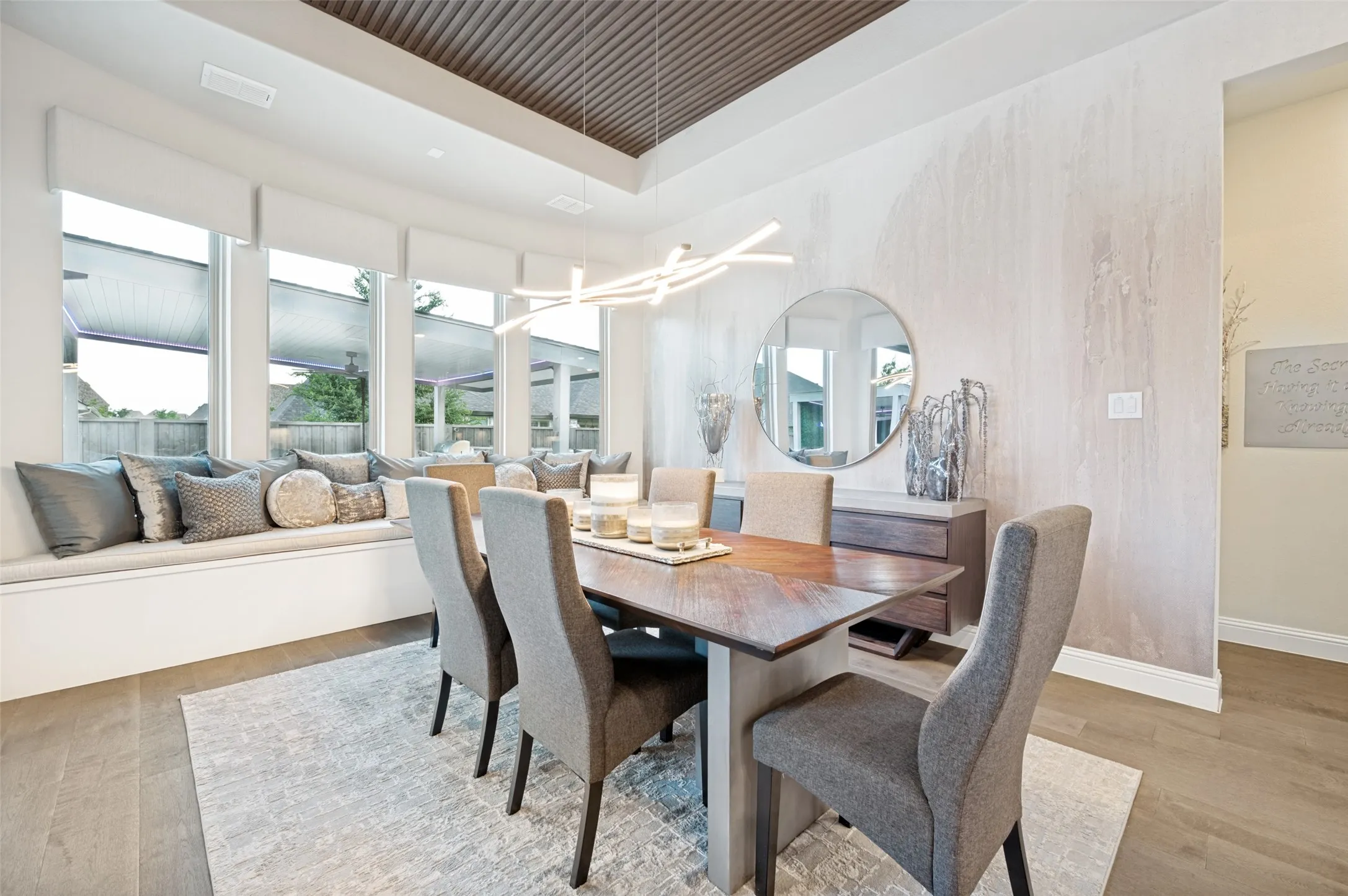 Spacious dining area featuring a custom window bench, large windows, wood-finish flooring, a contemporary linear light fixture, and a decorative ceiling treatment